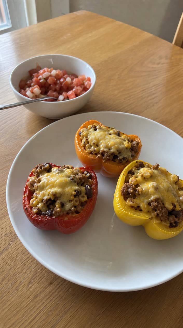 Bell peppers stuffed with ground chicken taco filling, melted cheese, and cilantro on a wooden board with fresh ingredients around.