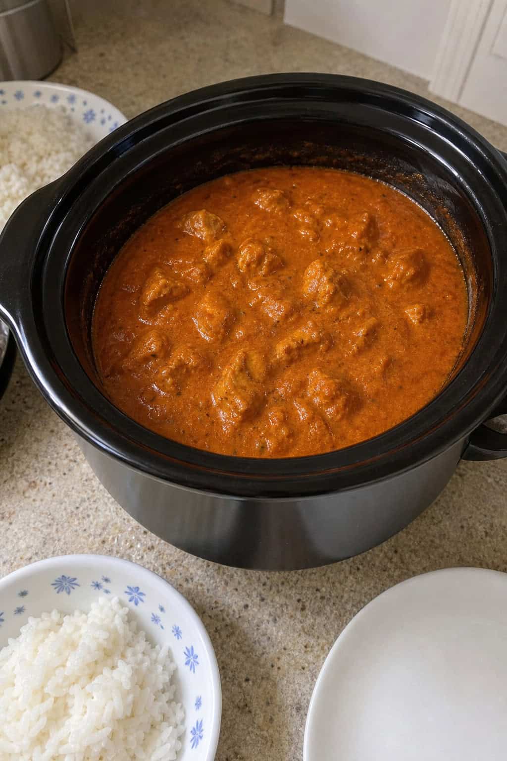 Slow cooker filled with Chicken Tikka Masala surrounded by fresh ingredients on a kitchen countertop.