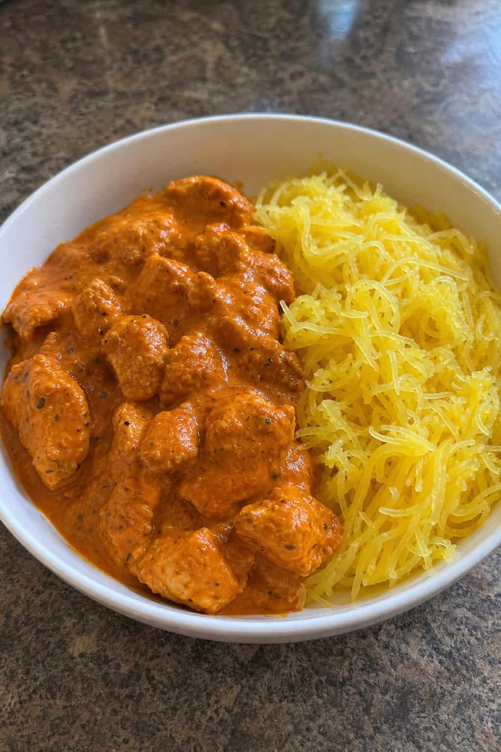 A plate of chicken tikka masala served with spaghetti squash on a wooden table.