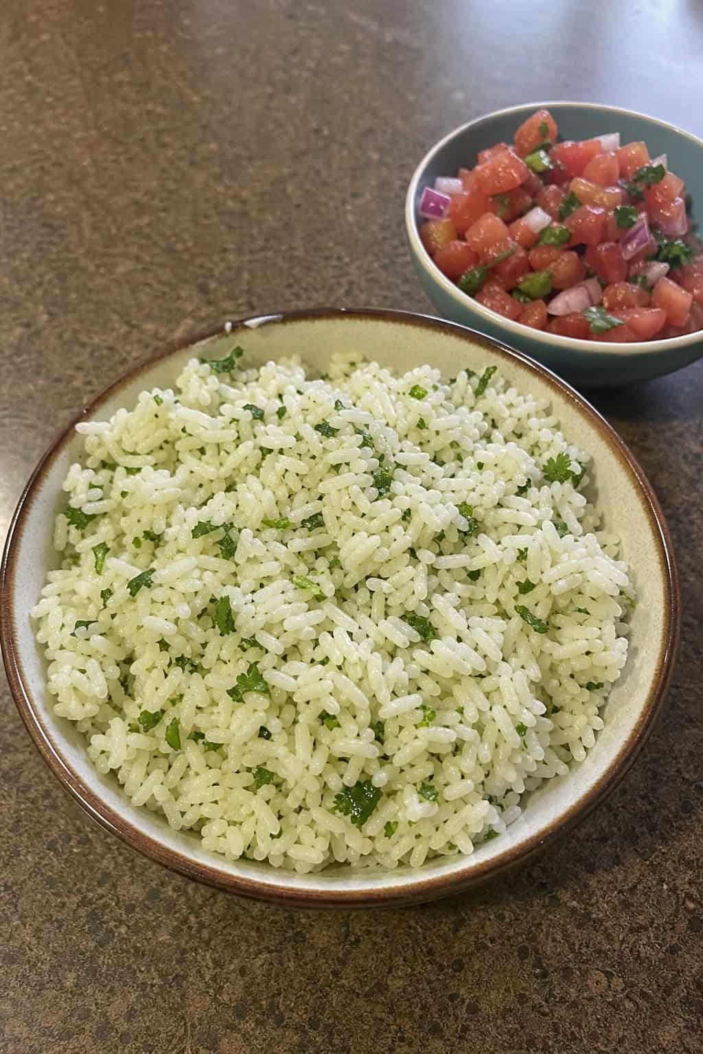A bowl of white rice mixed with chopped cilantro and lime zest on a wooden table with lime wedges and cilantro sprigs nearby.