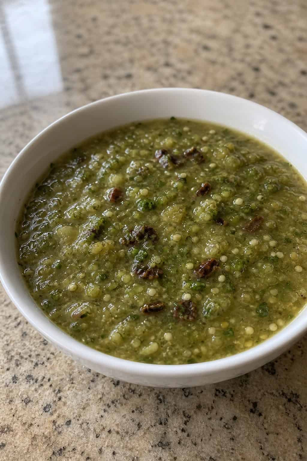 A bowl of green salsa verde surrounded by fresh tomatillos, lime wedges, garlic, and cilantro on a wooden surface.