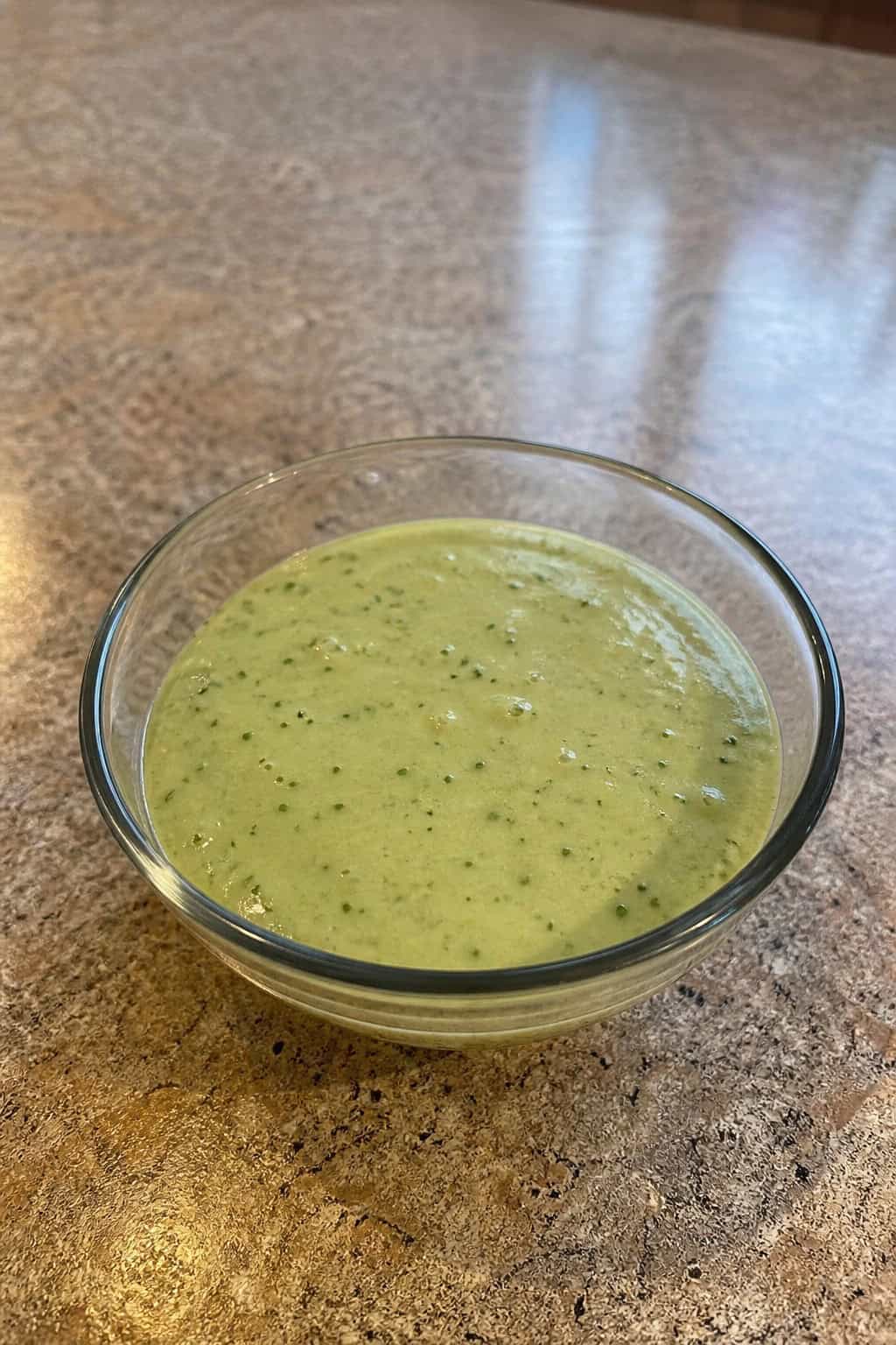 A bowl of creamy green tomatillo dressing surrounded by fresh tomatillos, jalapeños, garlic, lime wedges, and cilantro on a wooden table.
