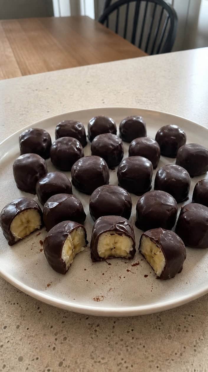 Chocolate-dipped frozen banana bites arranged on a wooden board outdoors during warm golden hour light.