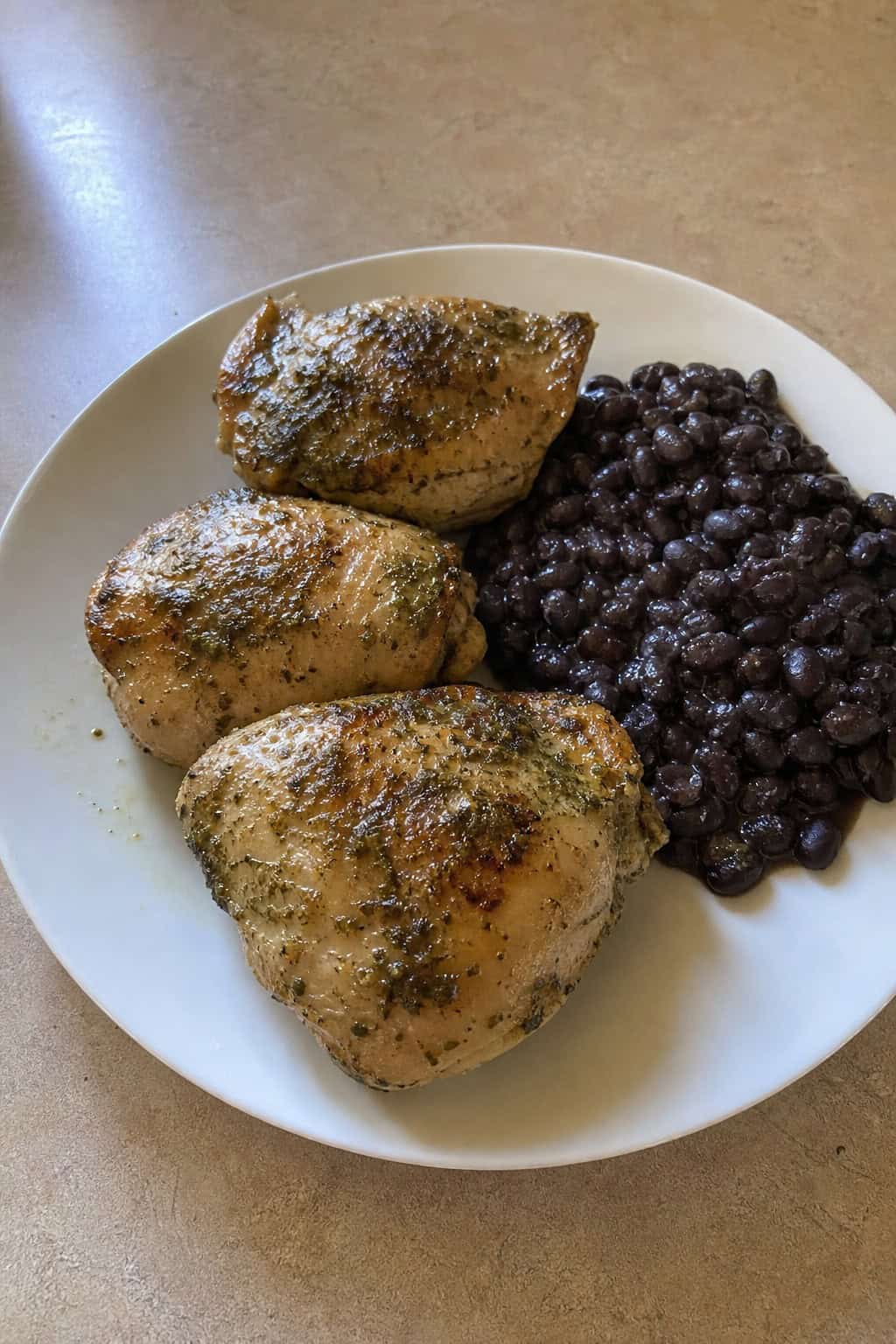 Sliced cilantro lime chicken thighs on a wooden table plated alongside glossy black beans, with fresh lime wedges and a handful of cilantro leaves arranged at the side.