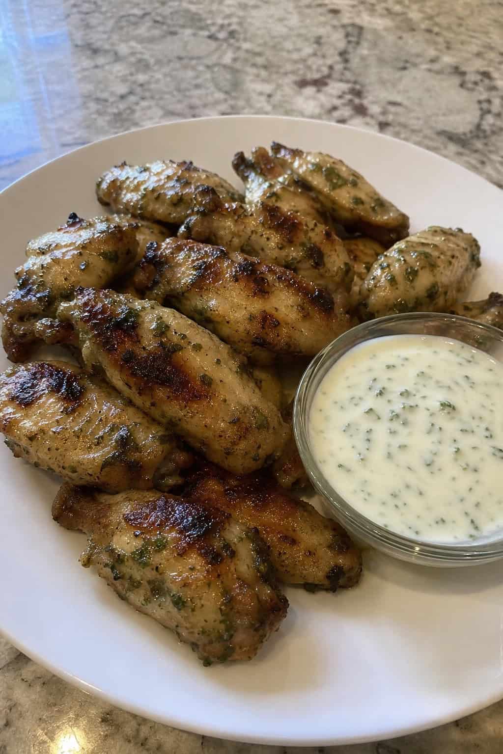 A plate of golden chicken wings garnished with cilantro and lime wedges, served with a small bowl of creamy lime sauce on a wooden table.