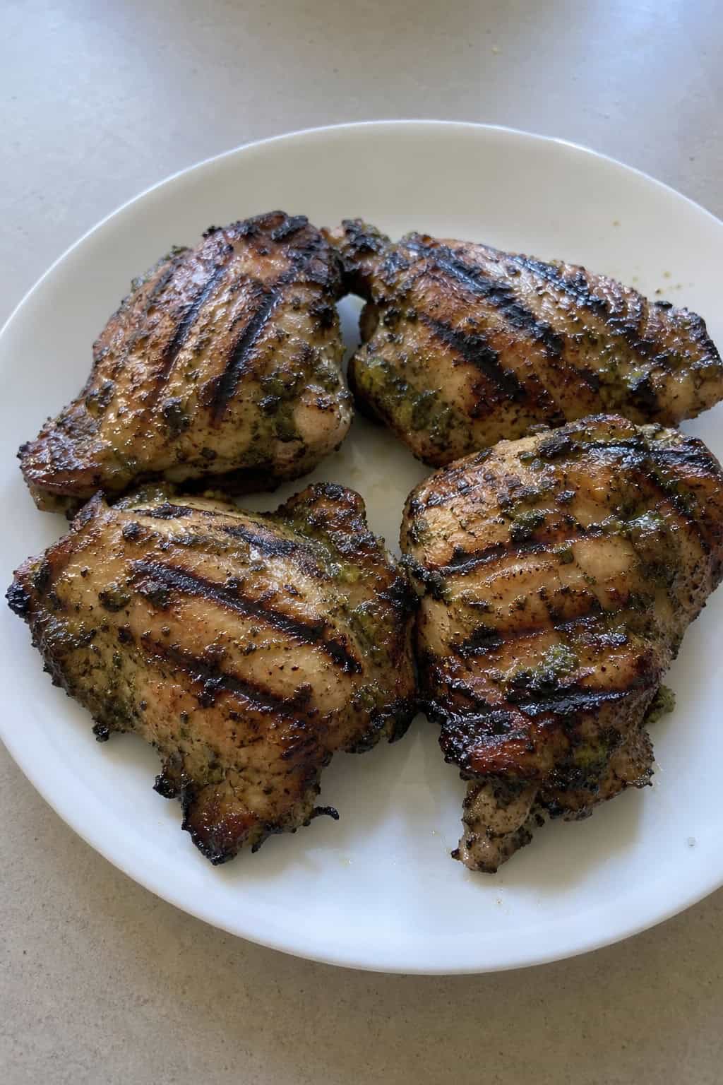 A plate of grilled chicken thighs garnished with fresh cilantro and lime wedges on a wooden table.