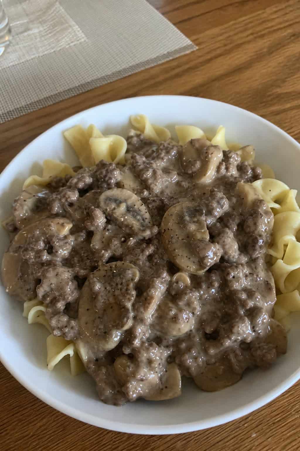 A bowl of beef and mushroom stroganoff with egg noodles on a wooden table, garnished with fresh parsley.