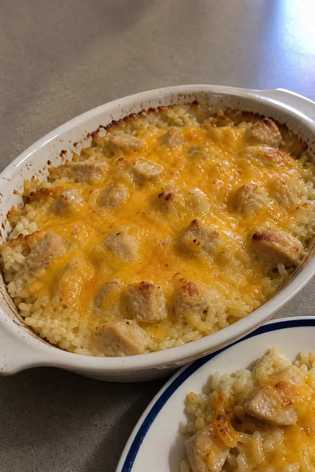 A freshly baked cheesy chicken and rice casserole in a golden ceramic dish on a wooden table, with a cracker-crumb topping and shredded cheddar visible on top.