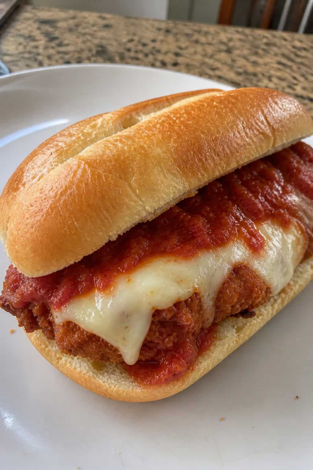 Close-up of a chicken parm sandwich with bubbling melted provolone and deep red marinara sauce on a toasted Italian roll
