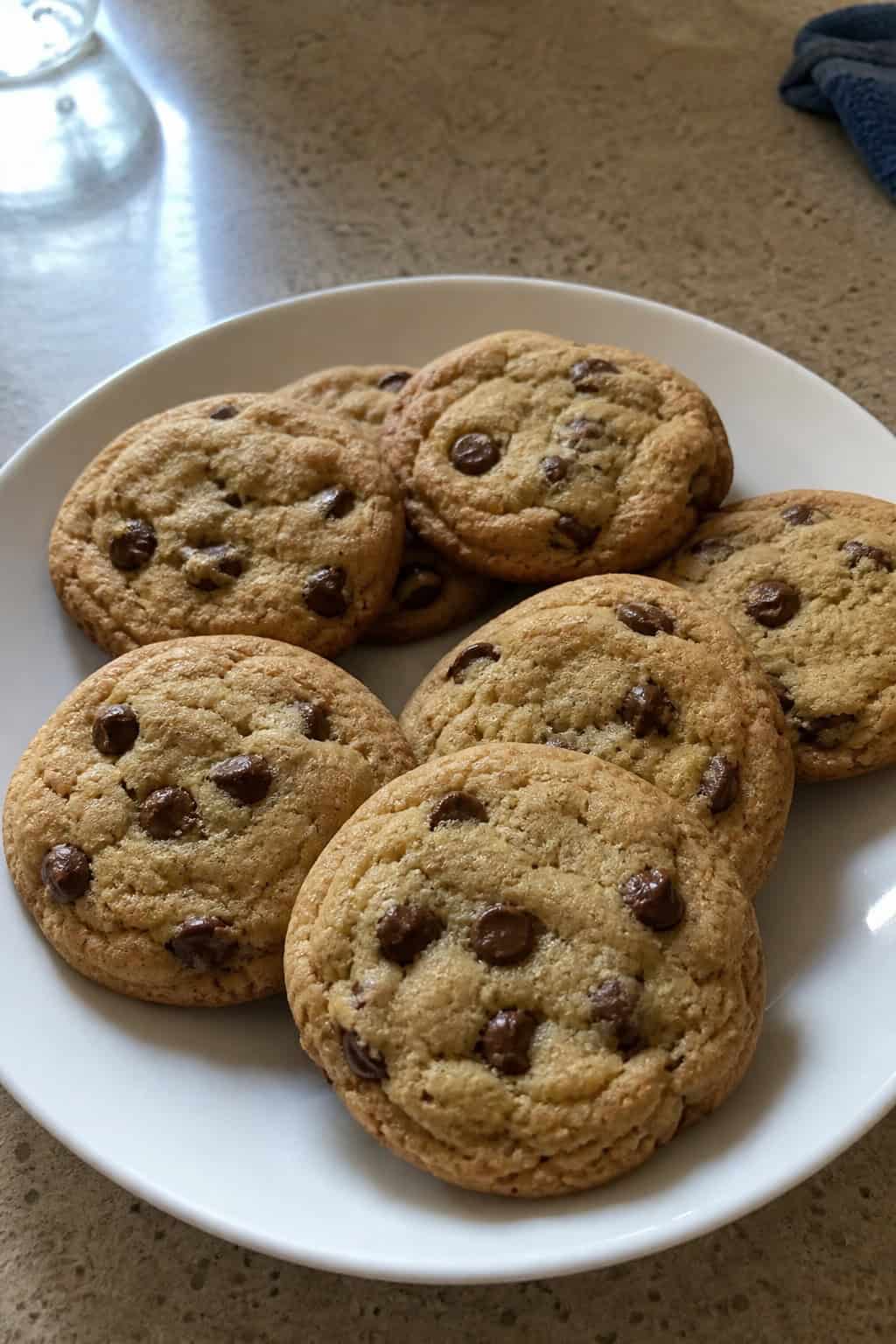 A close-up of freshly baked chocolate chip cookies on a wooden table with a glass of milk in the background.