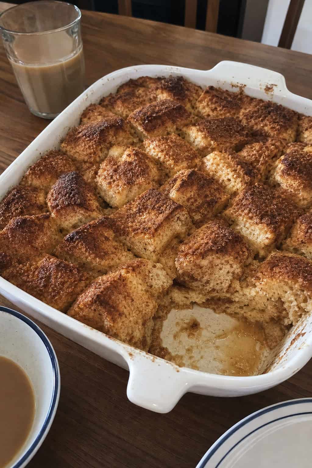 A cinnamon-stuffed French toast casserole in a golden-brown baking dish on a wooden table with a small pitcher of syrup and a handful of fresh berries alongside.