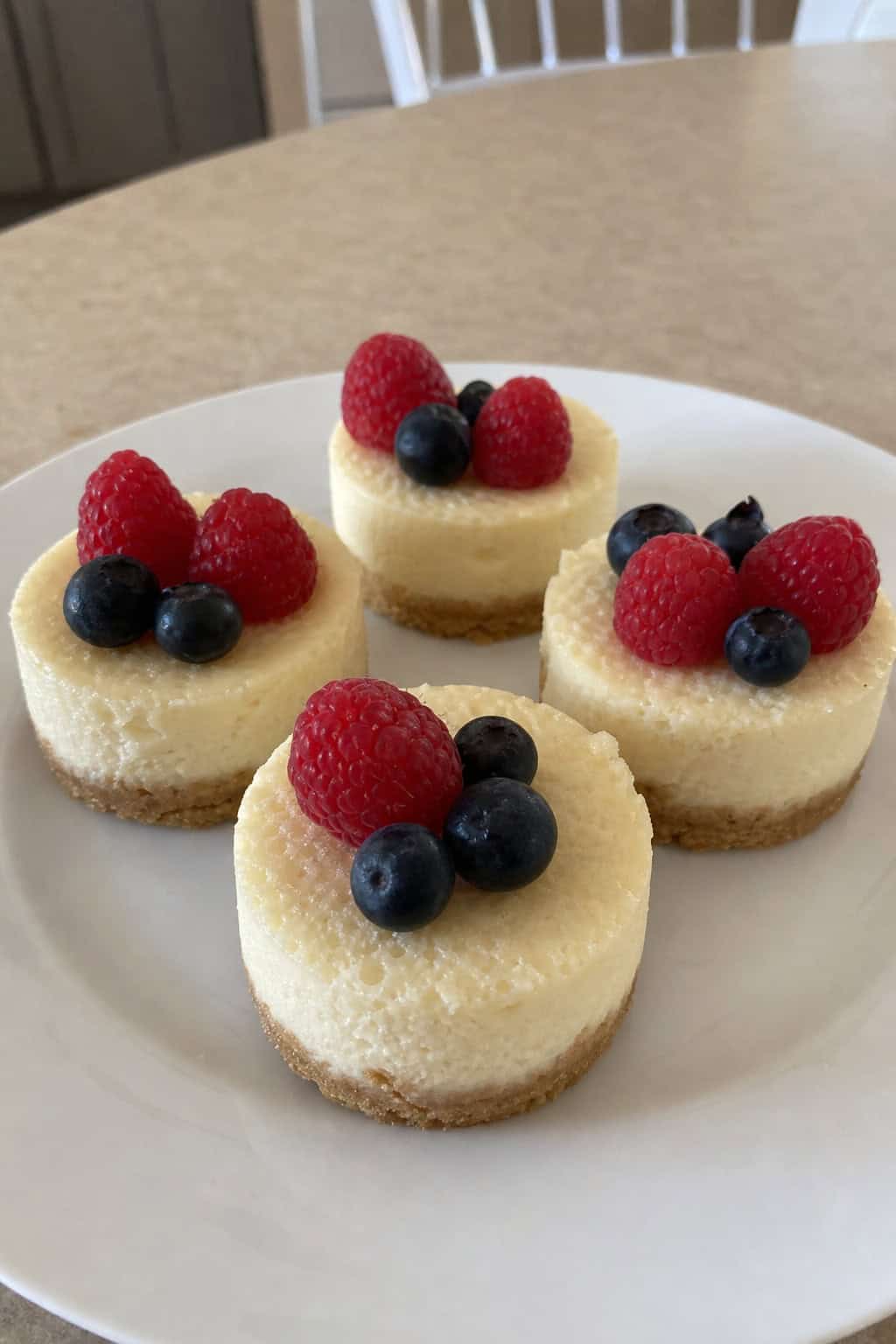 Close-up of several mini cheesecakes with graham cracker crusts topped with fresh berries on a wooden board.