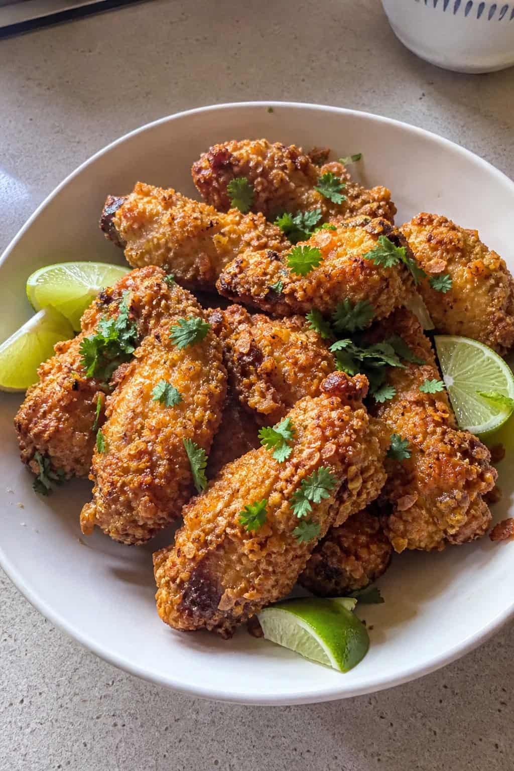 A plate of crispy coconut curry chicken wings garnished with cilantro and lime wedges on a wooden table.