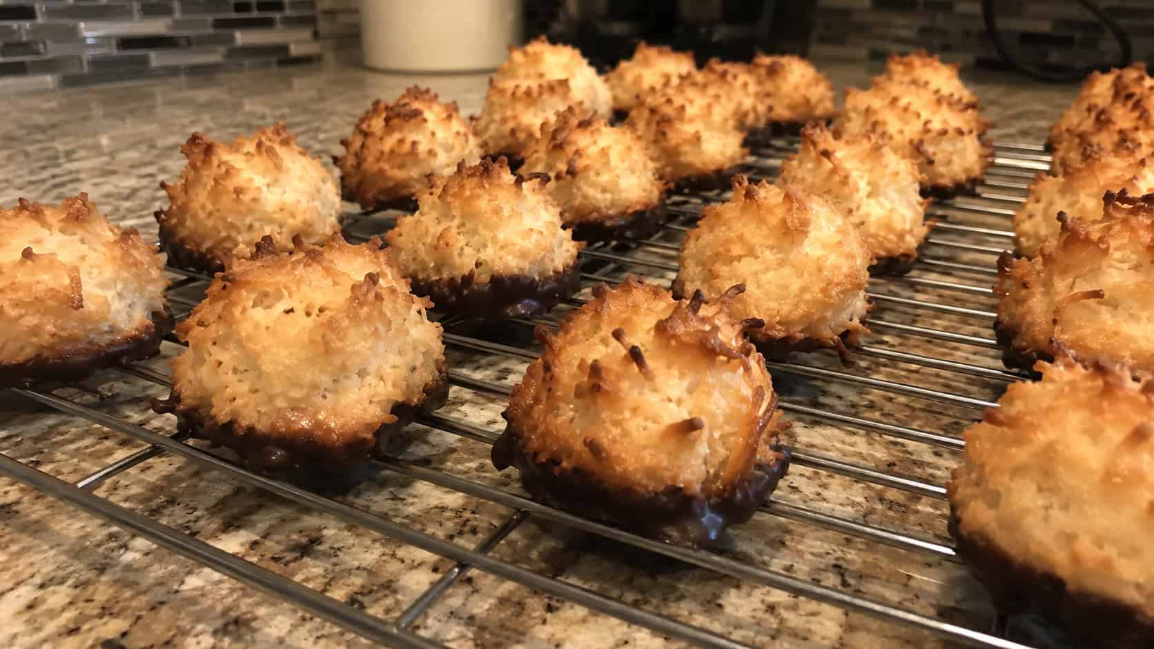 finished coconut macaroons on a wire cooling rack, craggy golden-brown toasted coconut mounds, several with chocolate-dipped bottoms, on a kitchen counter in warm natural light, casual home baking