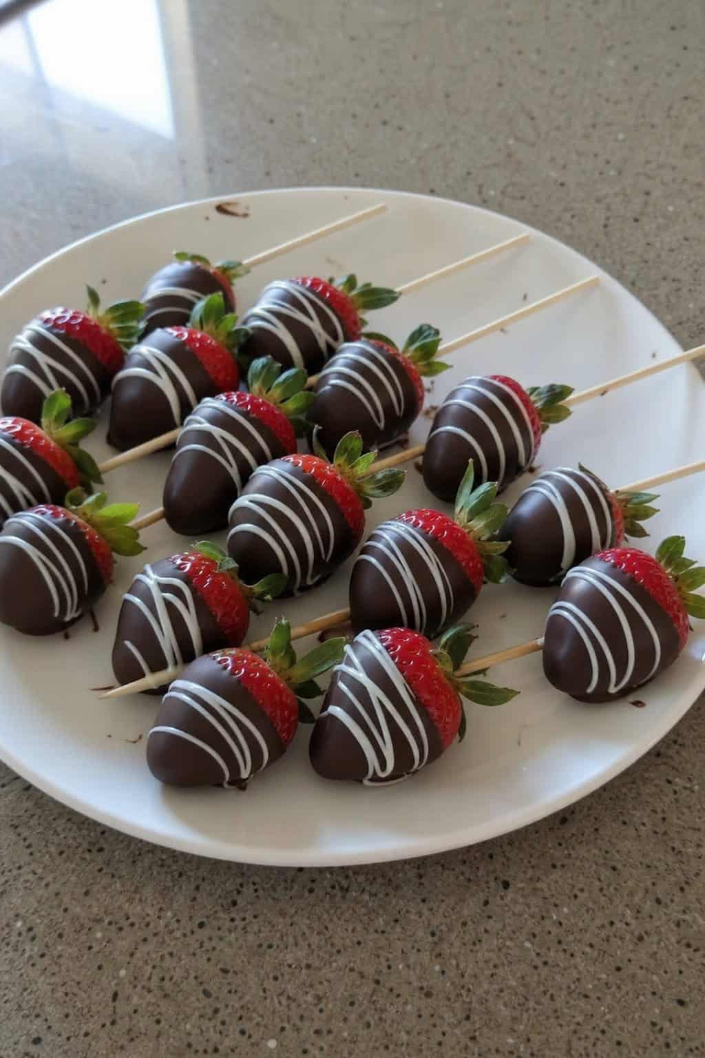 Close-up of chocolate-covered strawberries on wooden skewers arranged on a serving board.