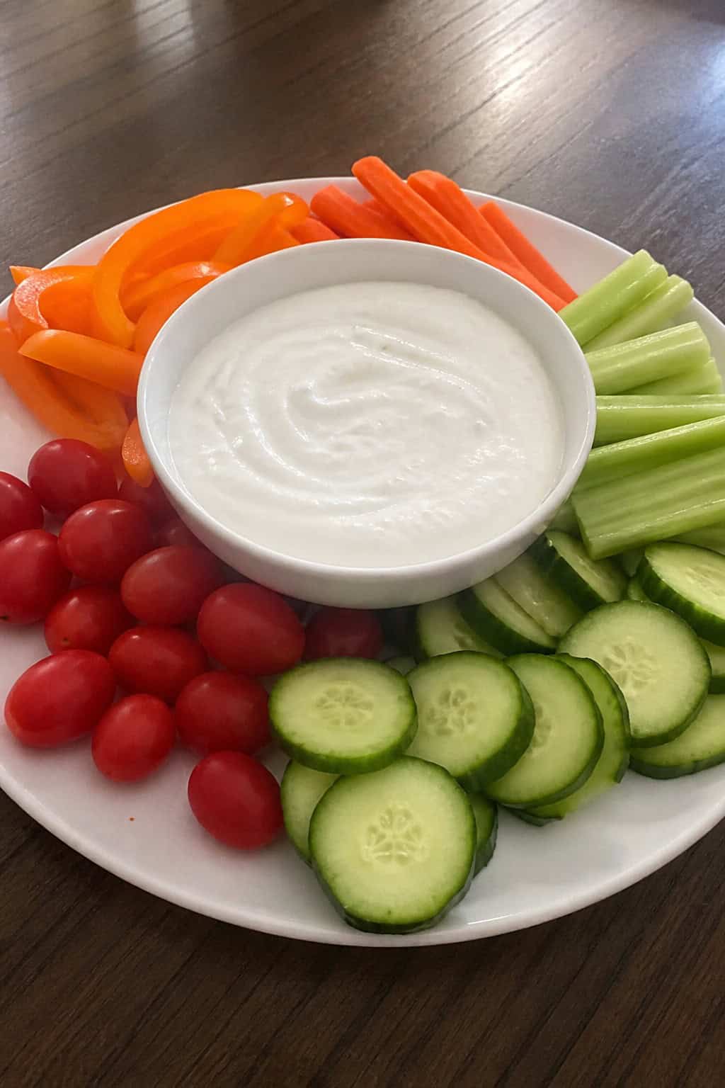 A bowl of Greek yogurt dip surrounded by an assortment of fresh vegetable sticks on a wooden table.