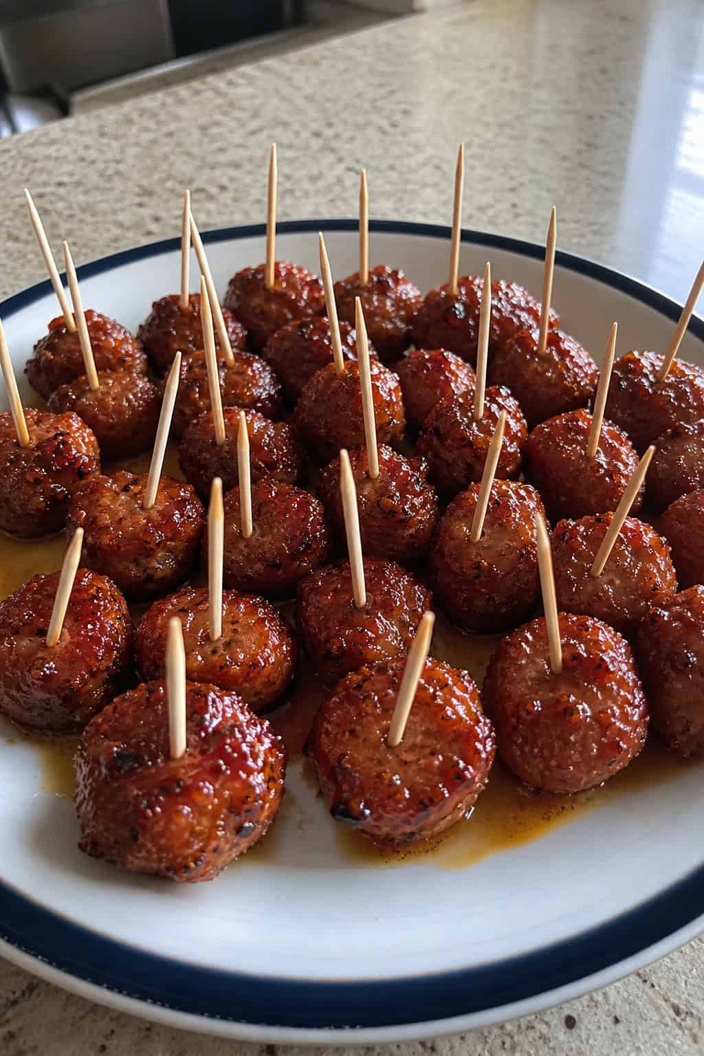 Close-up of honey-glazed sausage bites on toothpicks arranged on a white serving platter.