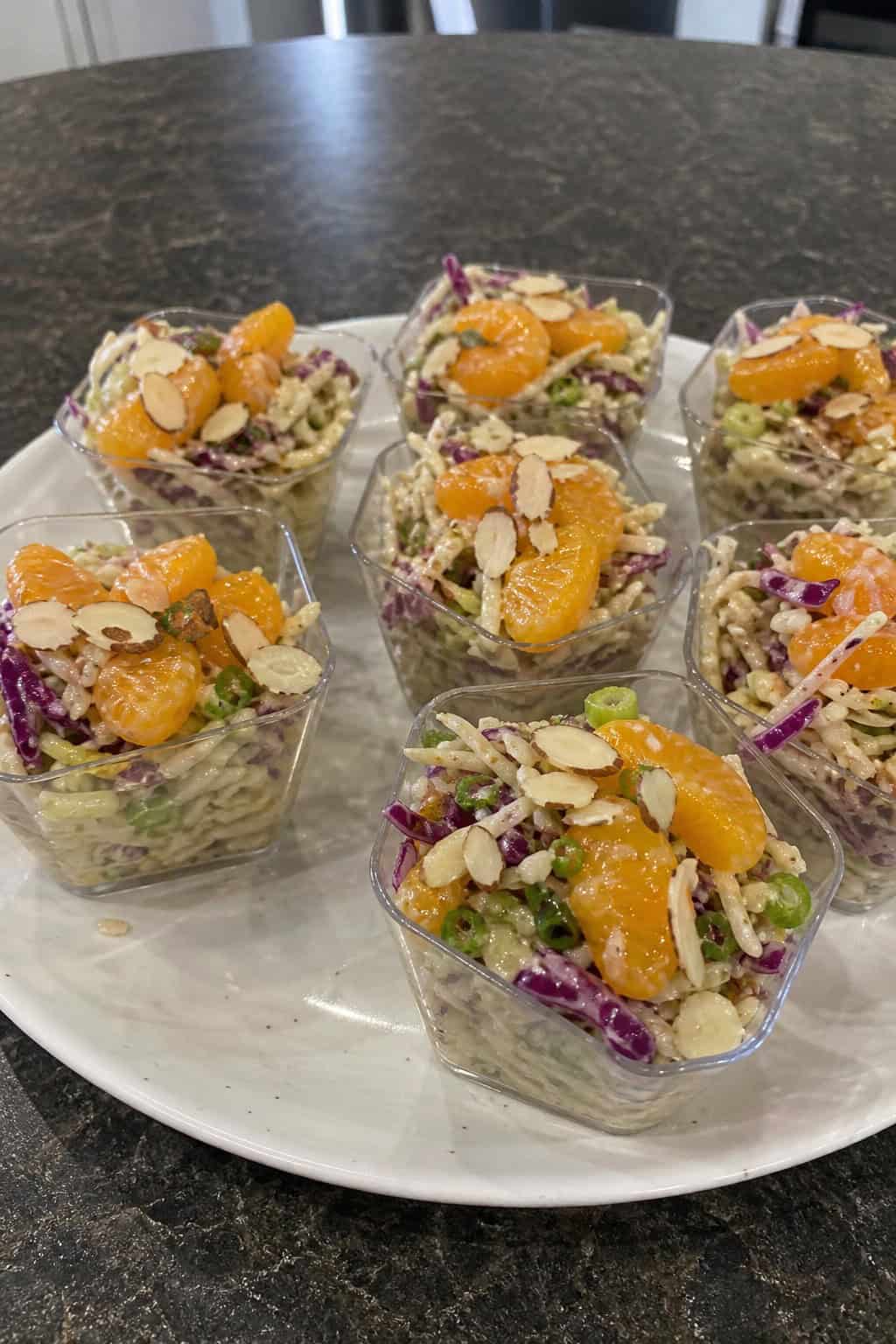Individual cups of Asian slaw with mandarin oranges and almonds arranged on a wooden serving board.