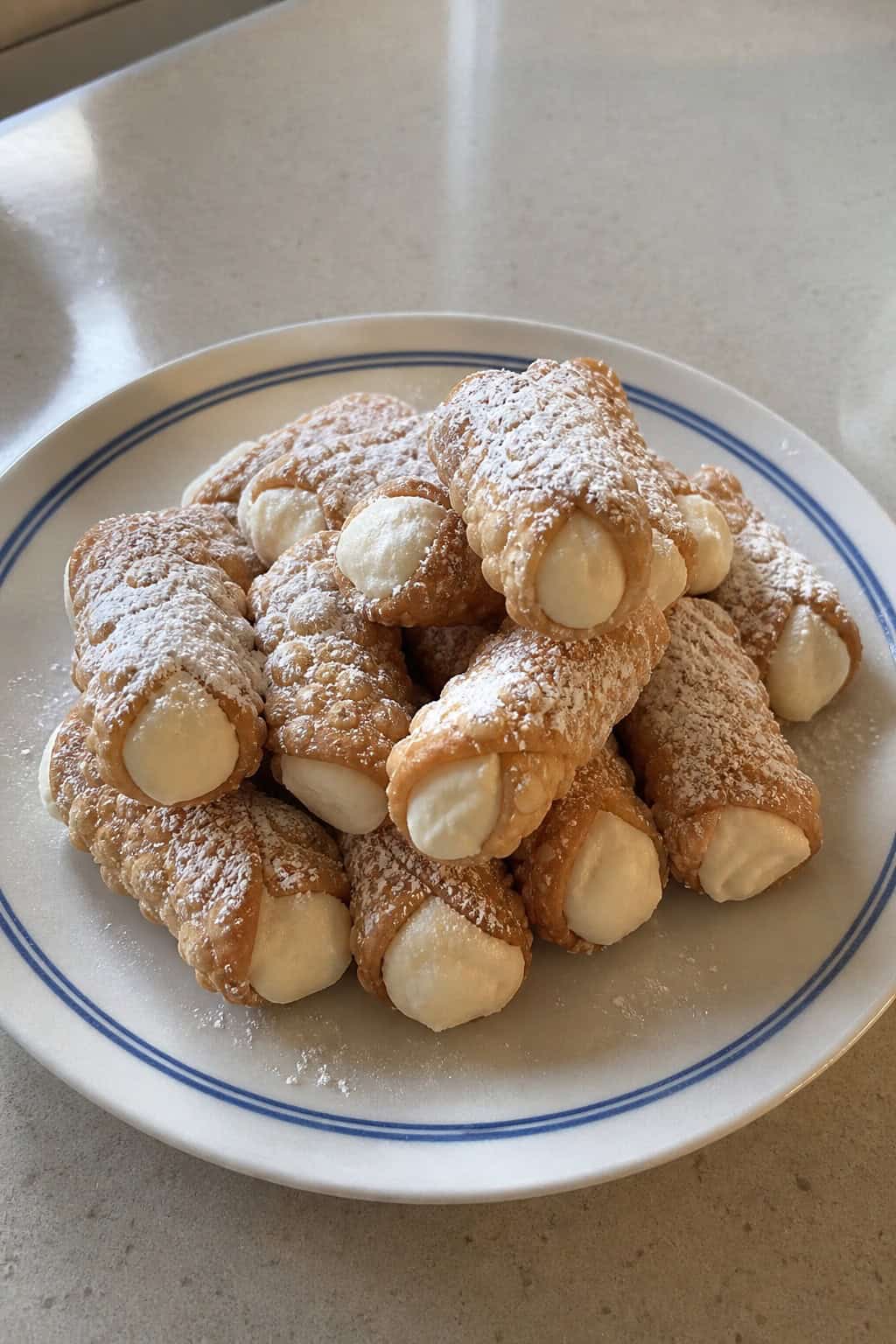 A plate of mini cannoli dusted with powdered sugar arranged on a wooden serving board.