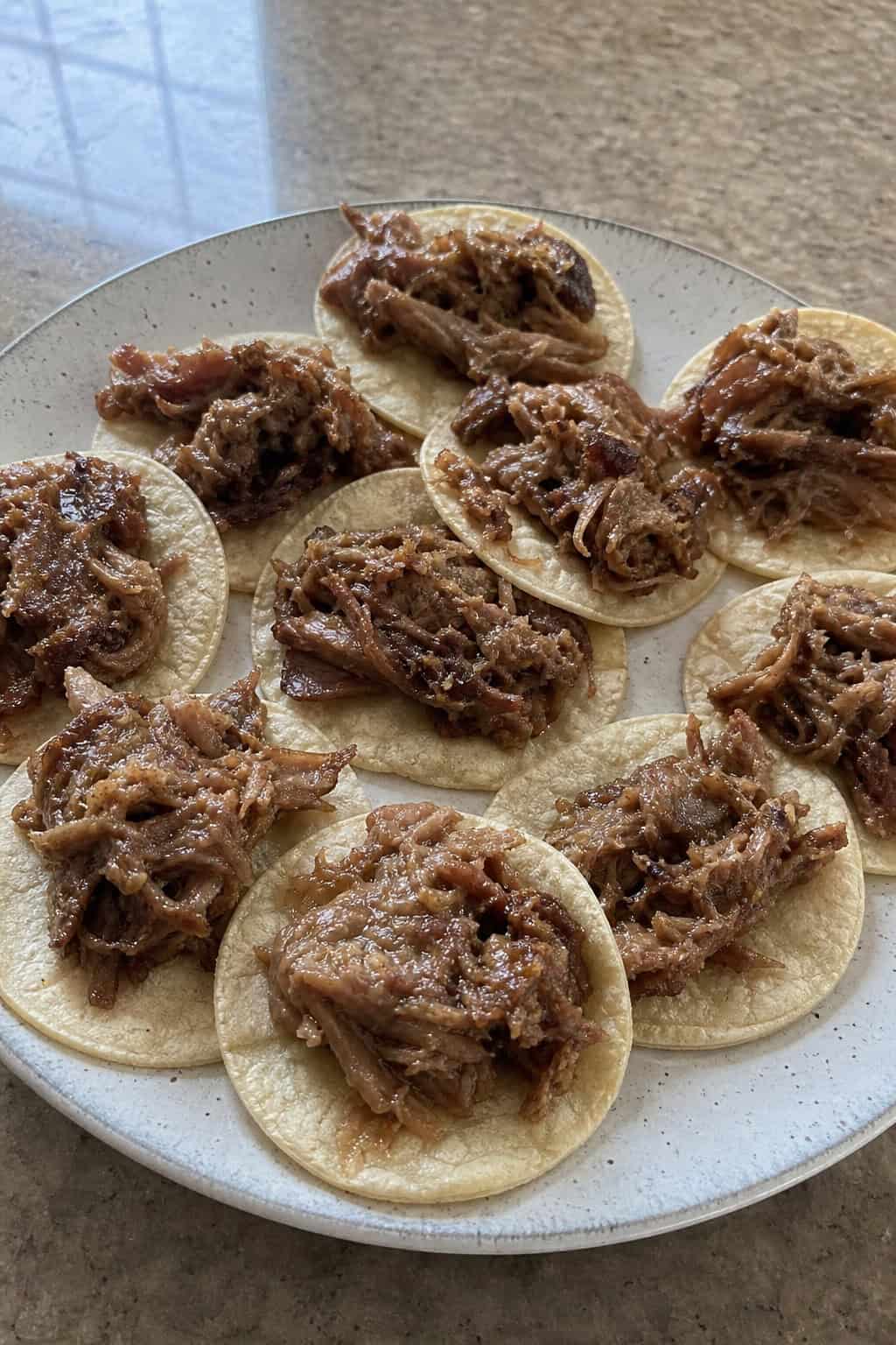 22 Easy Costco Party Appetizers 12 Mini street tacos filled with shredded carnitas, topped with cilantro and onions, arranged on a wooden platter with bowls of salsa and guacamole nearby.