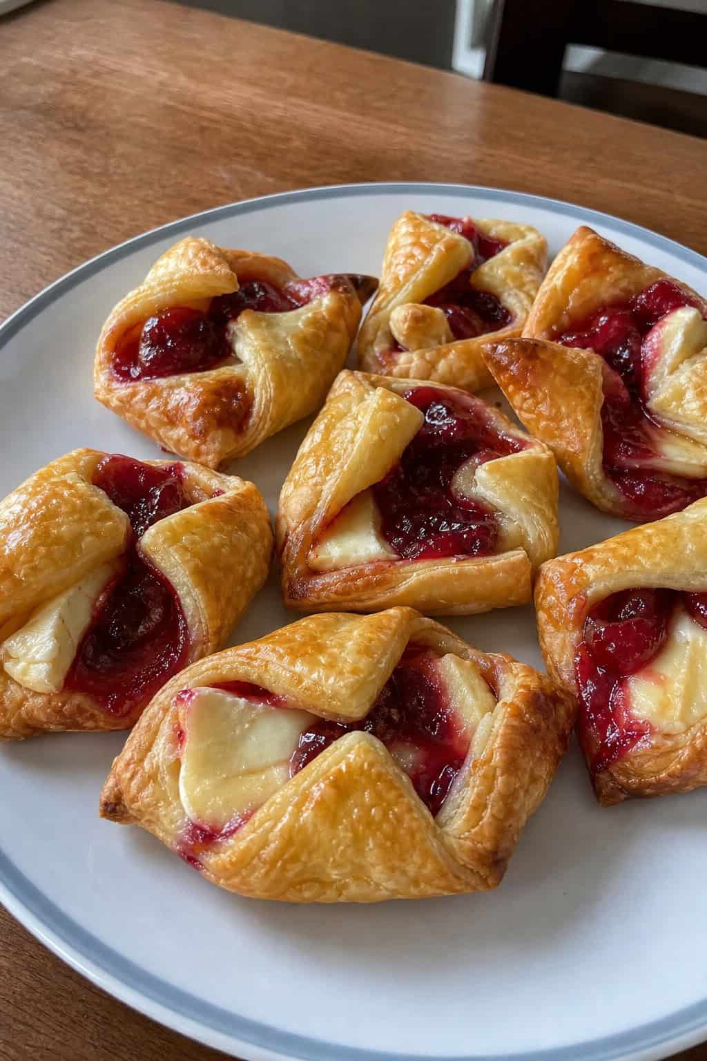 Close-up of golden cranberry brie puff pastry bites on a wooden board with a festive table setting in the background.