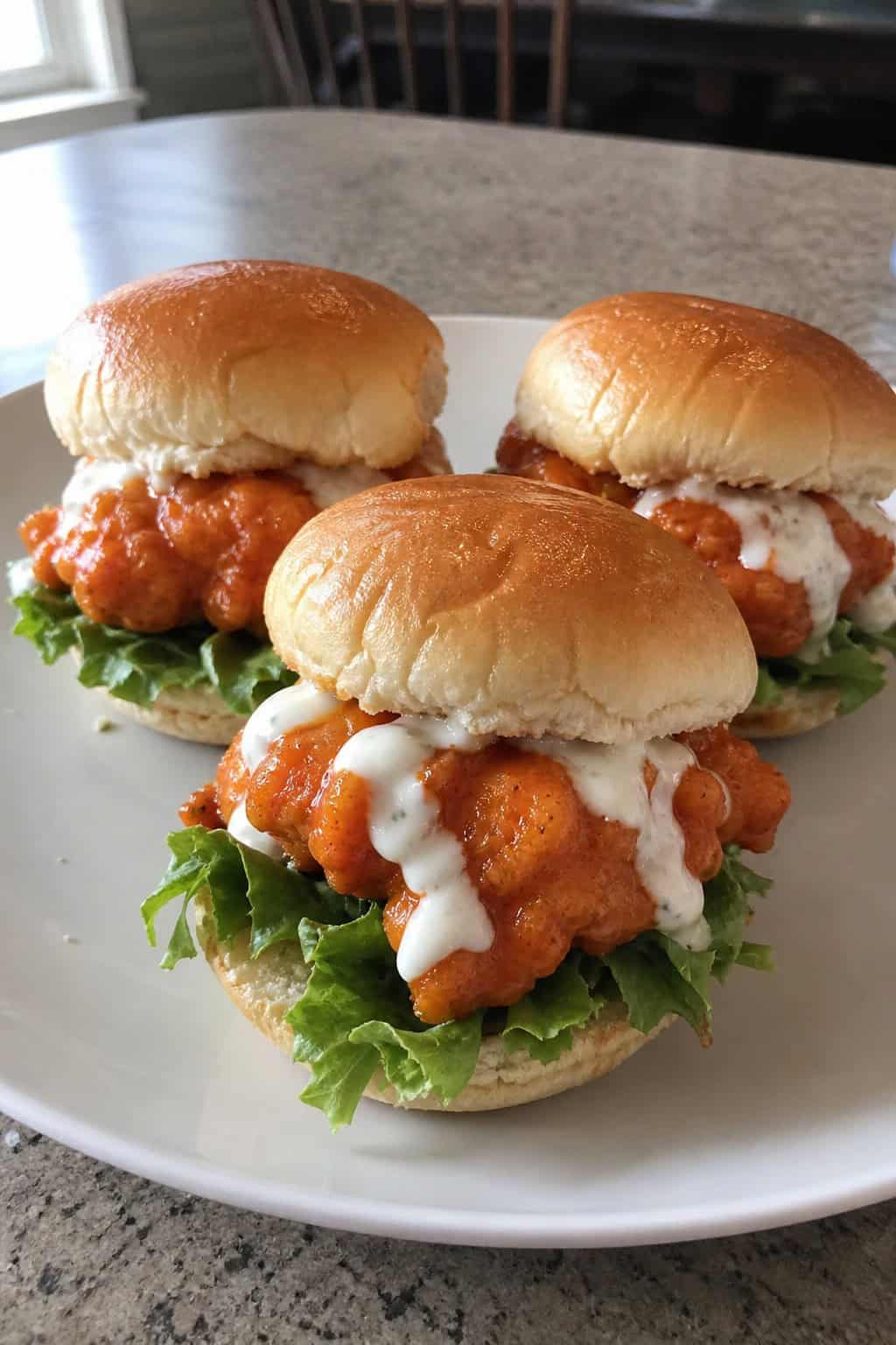 Close-up of buffalo ranch chicken wing sliders with lettuce on a wooden board, served with celery, carrot sticks, and a bowl of ranch dressing.