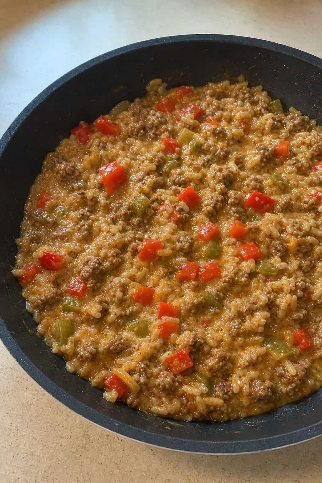 A skillet filled with creamy Cajun beef and rice garnished with chopped parsley on a wooden table.