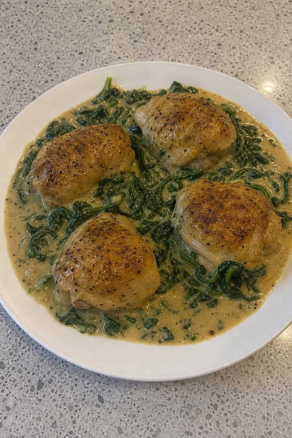A plate of baked chicken thighs covered in creamy Dijon sauce with spinach, garnished with fresh herbs on a wooden table.
