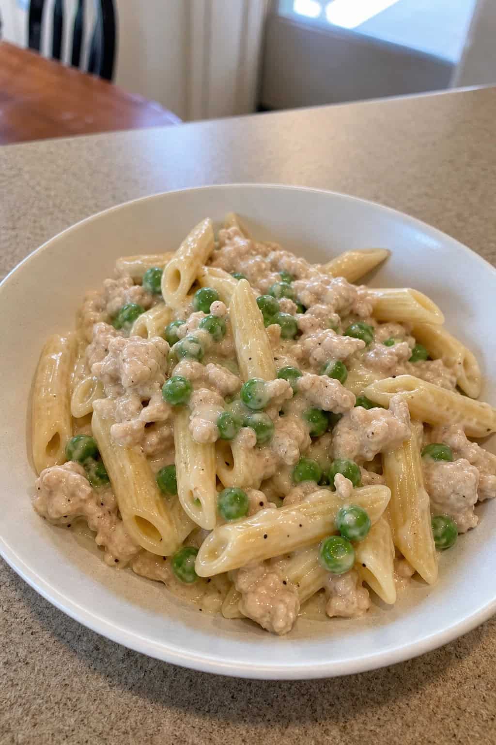 A bowl of creamy minced chicken and pea pasta garnished with fresh herbs on a wooden table.