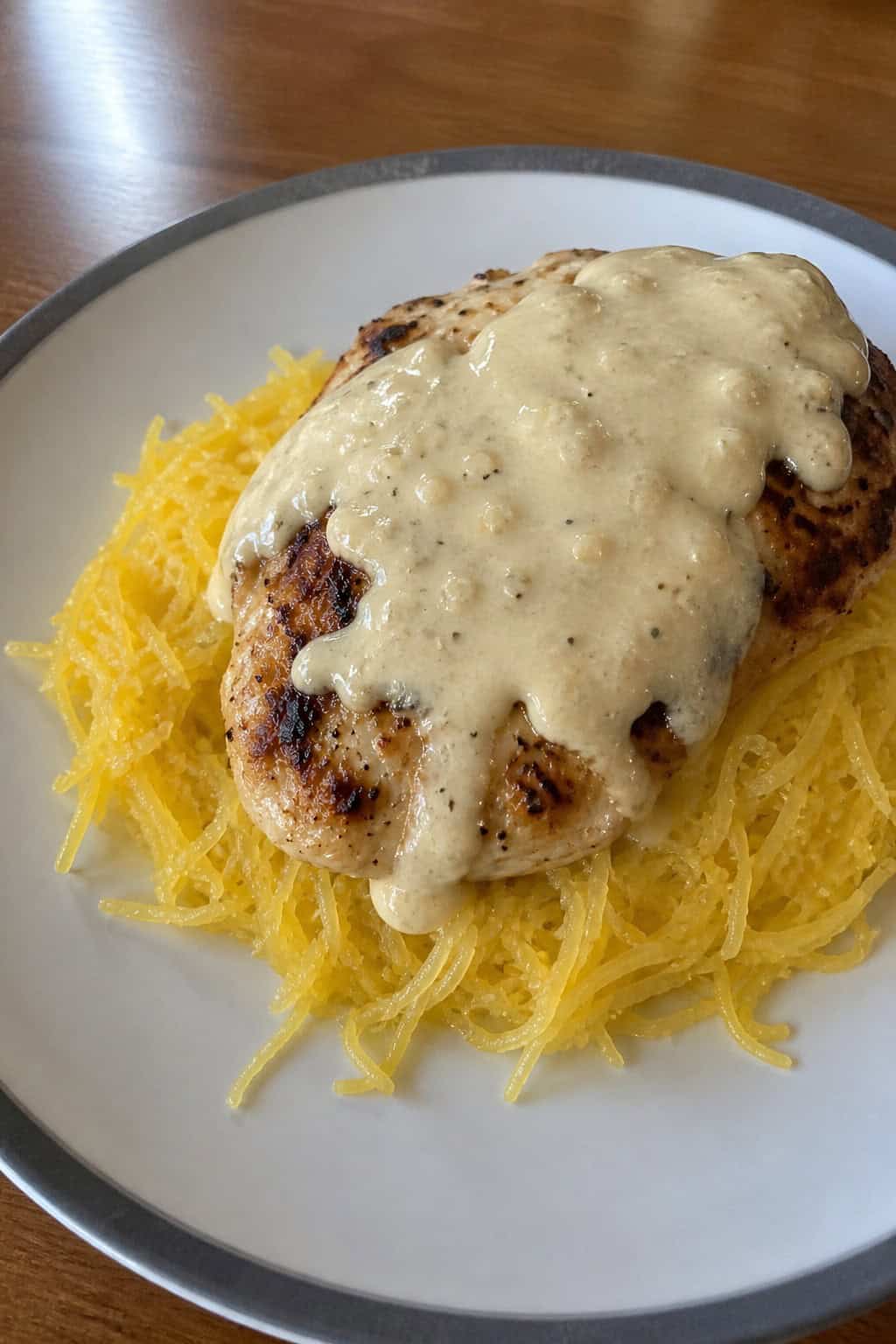 A plate of creamy garlic parmesan chicken served over spaghetti squash garnished with fresh herbs on a wooden table.