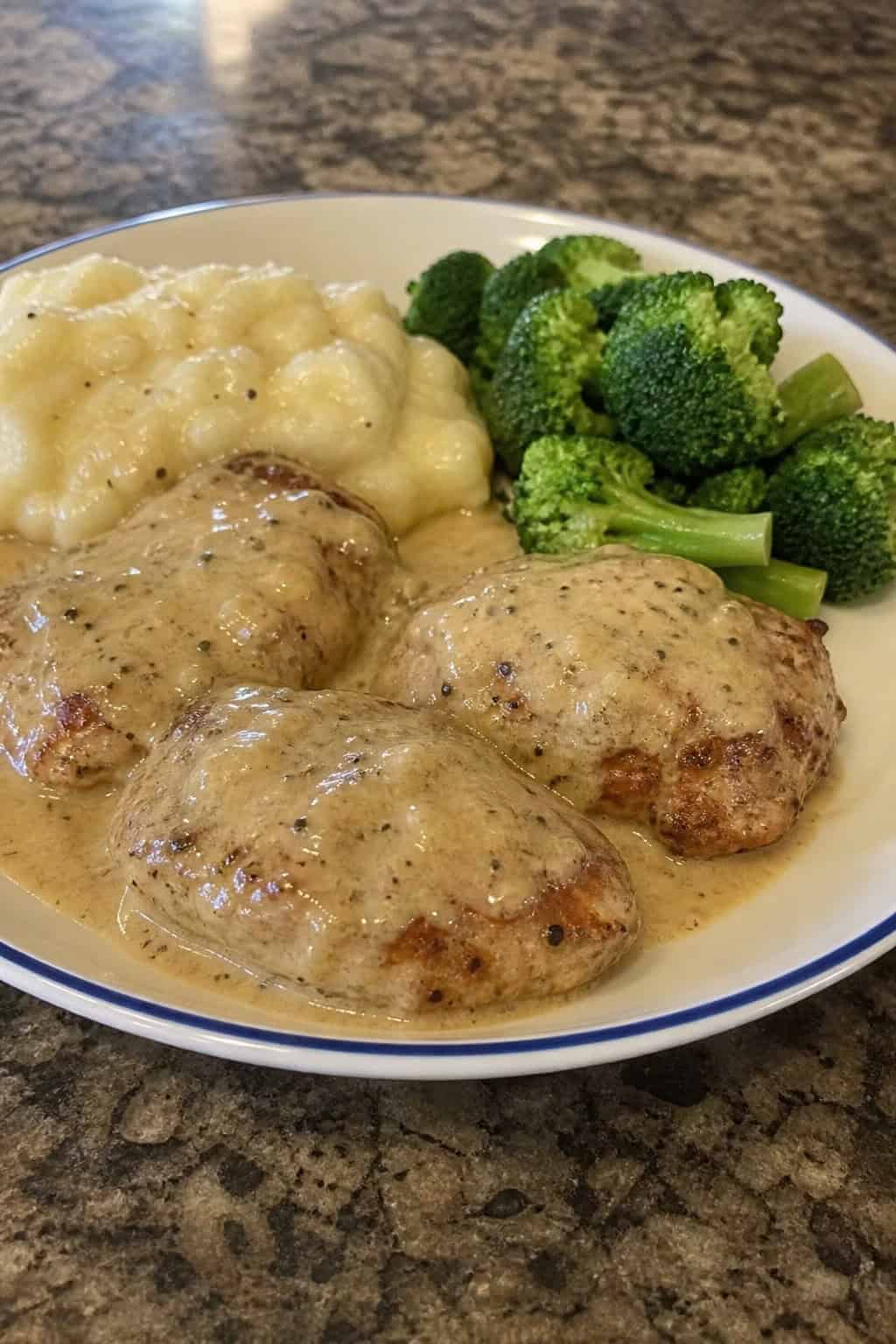 Plate of creamy garlic parmesan chicken thighs with green vegetables and mashed potatoes on a kitchen table.