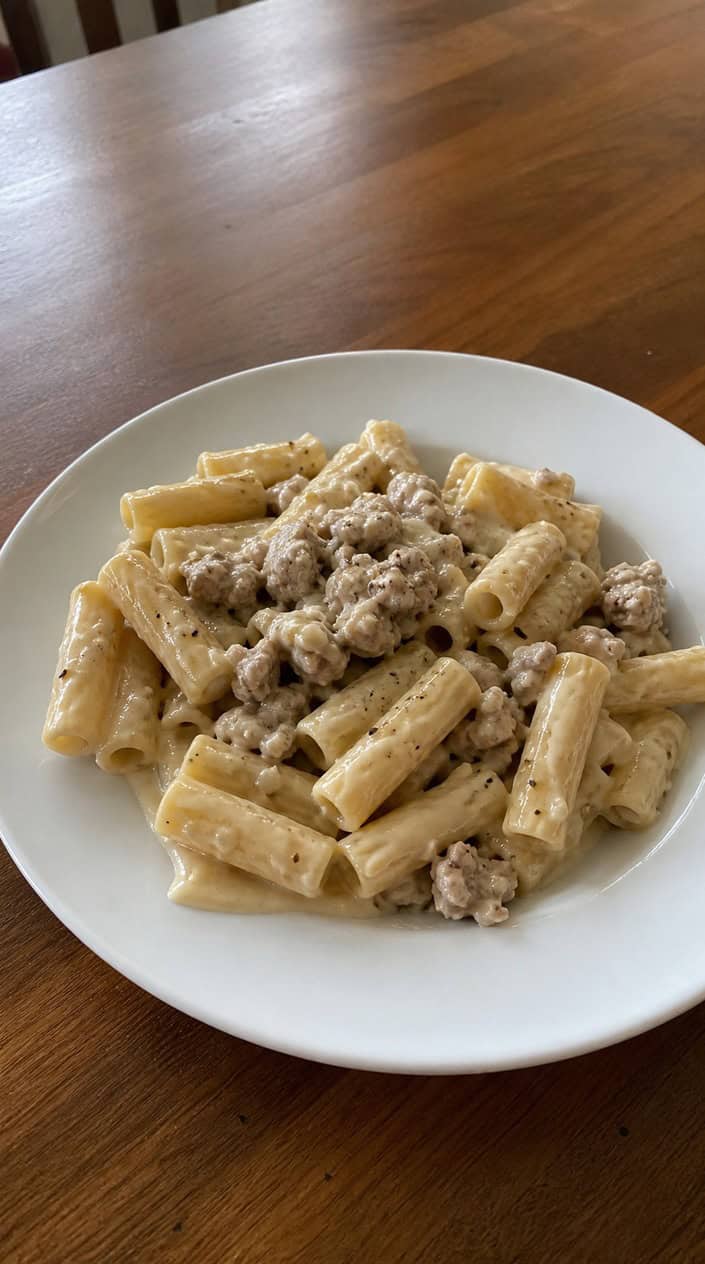 A bowl of creamy lemon-garlic ground chicken pasta garnished with parsley on a wooden table with lemon halves and garlic cloves nearby.