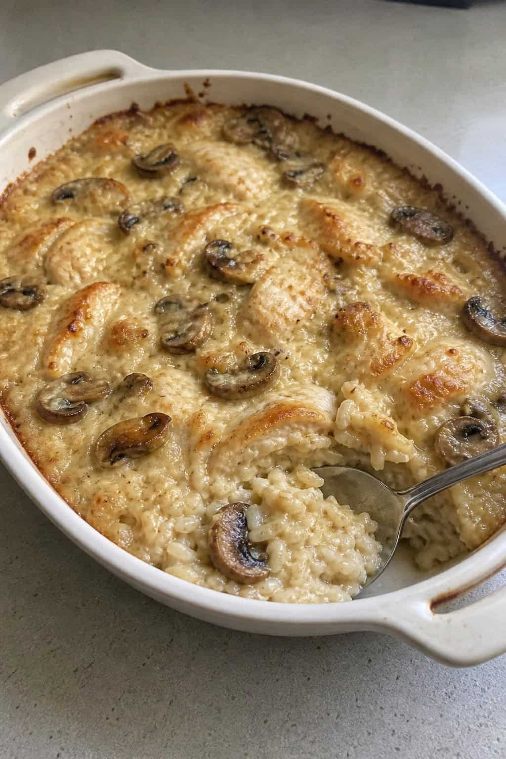 A freshly baked creamy mushroom and chicken rice casserole in a ceramic dish on a wooden table with sliced cremini mushrooms and fresh thyme sprigs nearby.