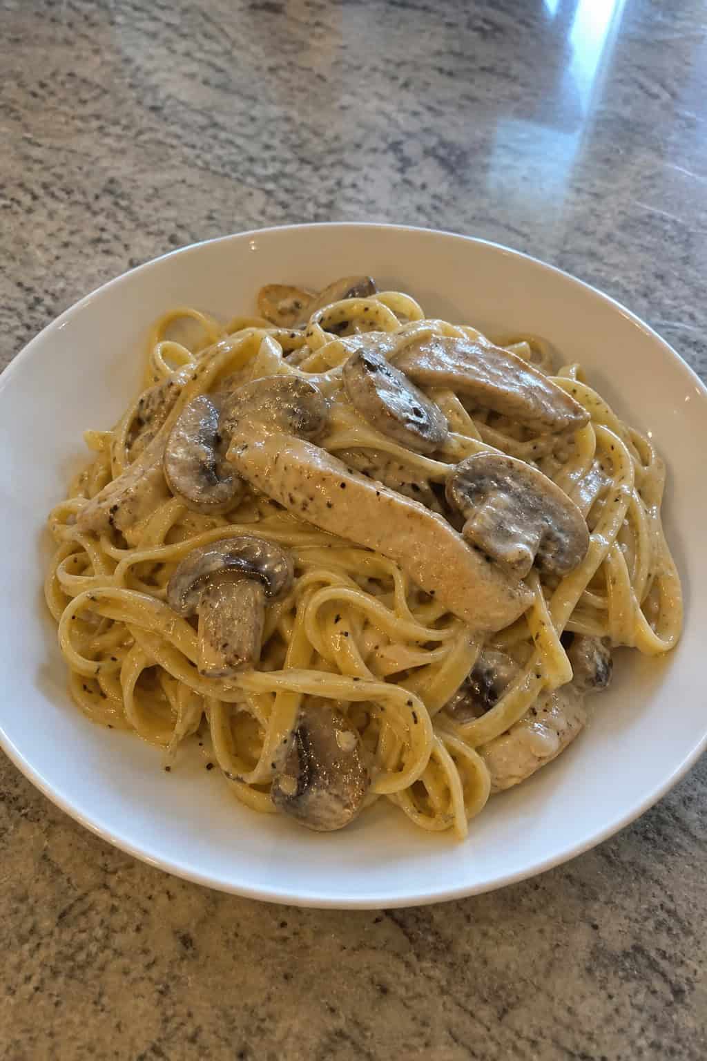 A bowl of creamy mushroom chicken stroganoff pasta garnished with parsley on a wooden table.