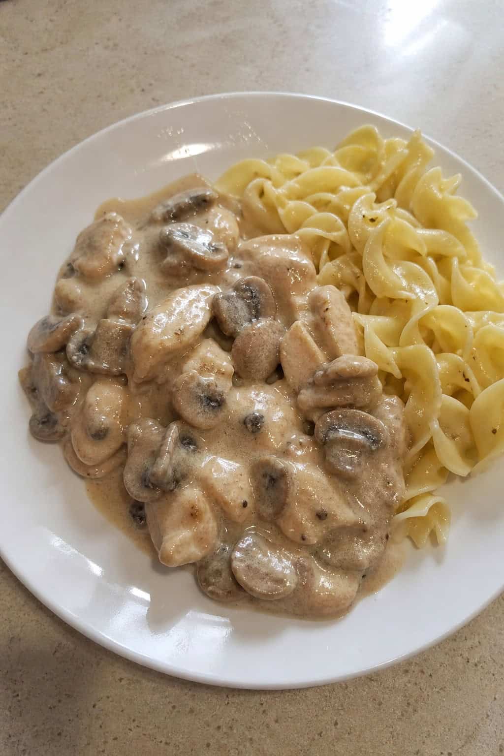 A bowl of creamy mushroom chicken stroganoff with egg noodles and parsley garnish on a wooden table.