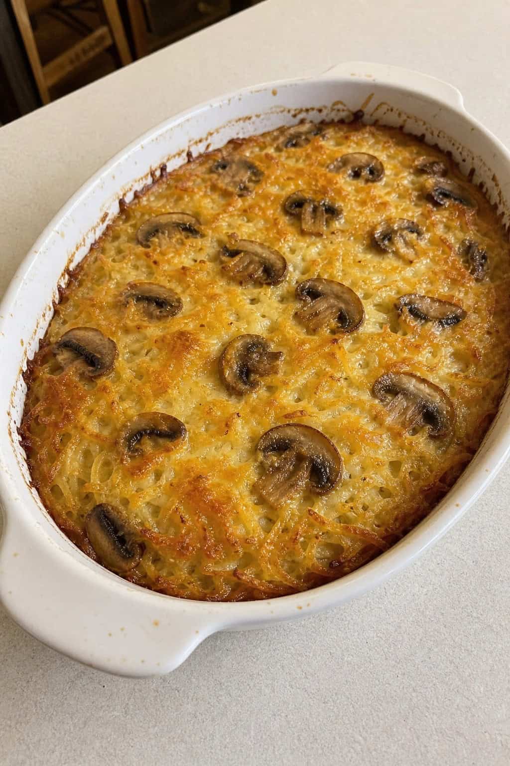 A creamy mushroom and thyme hashbrown casserole in a rustic baking dish on a wooden table with fresh thyme and a wooden spoon nearby.