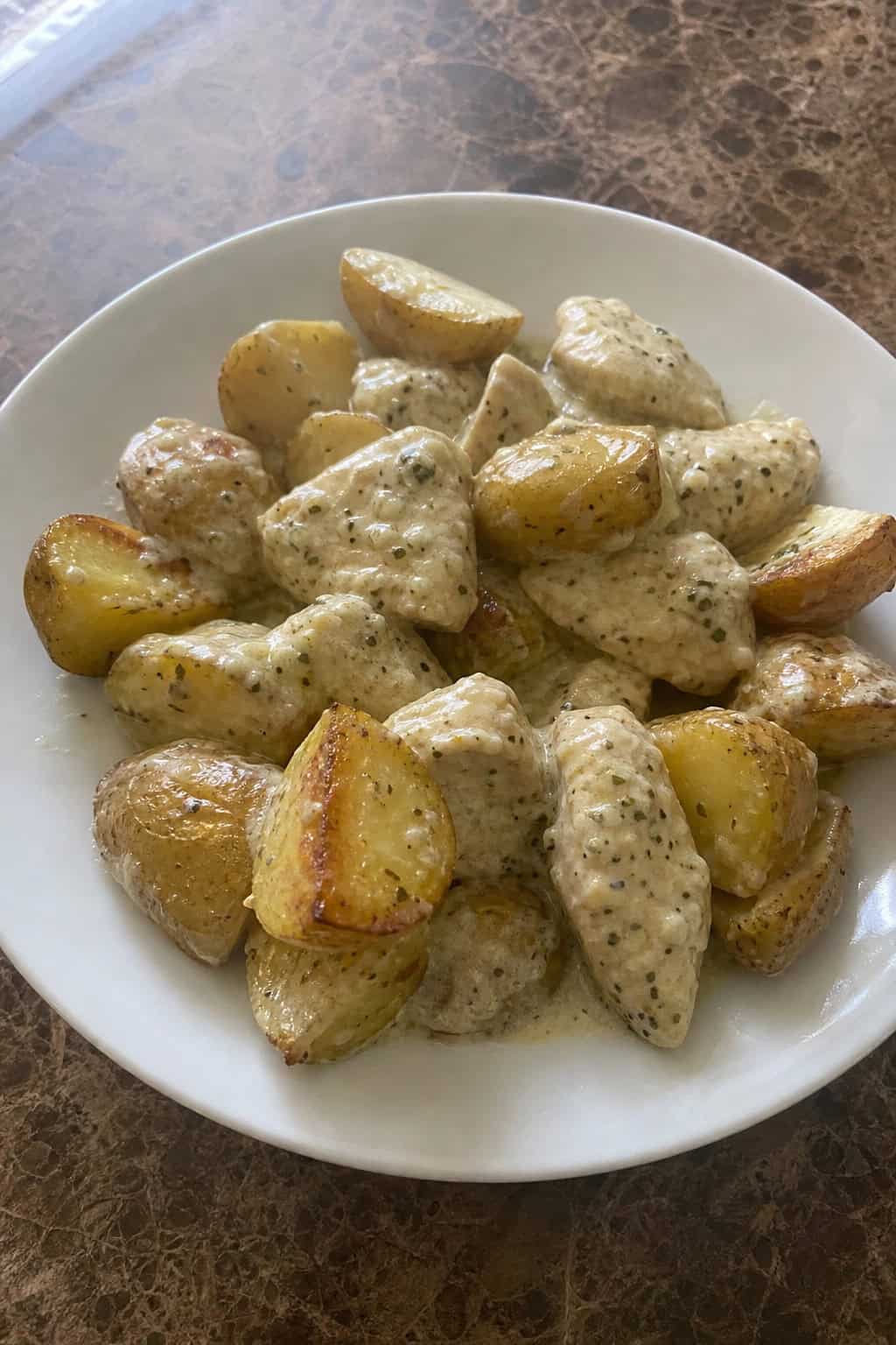 A bowl of creamy ranch chicken with roasted potatoes garnished with fresh herbs on a wooden table.
