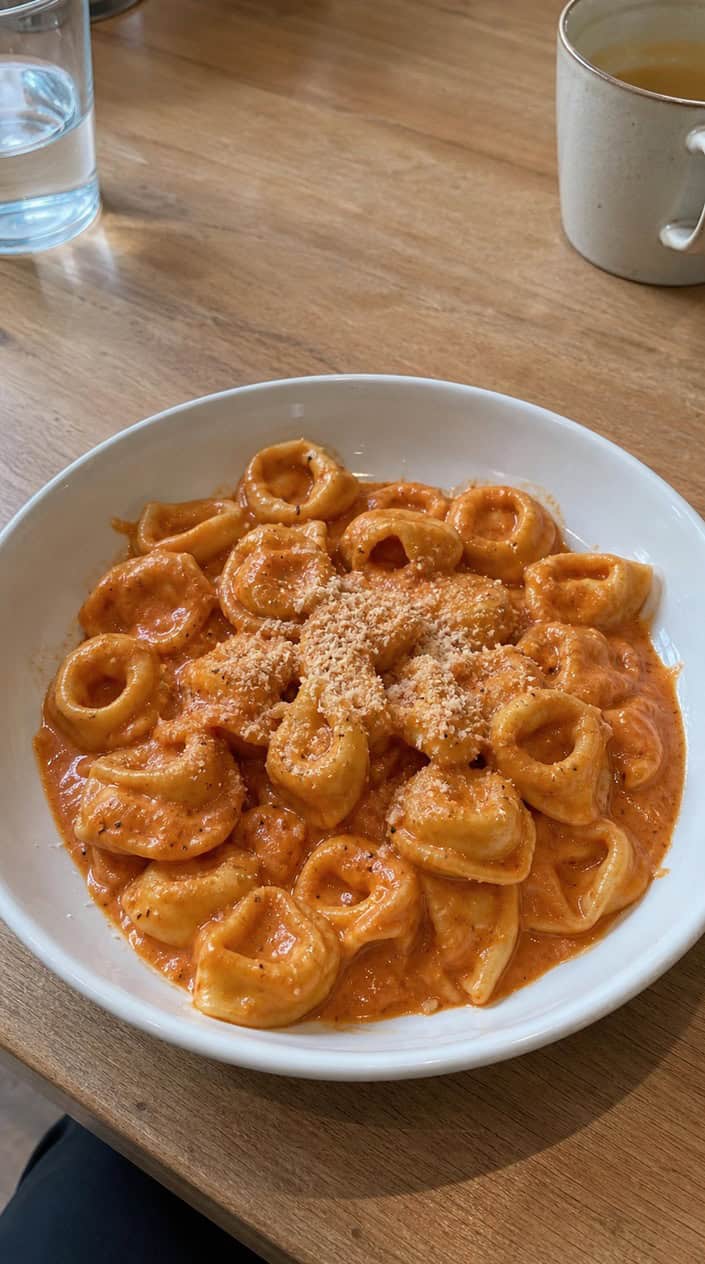 A bowl of creamy tomato tortellini pasta garnished with fresh basil on a wooden table.