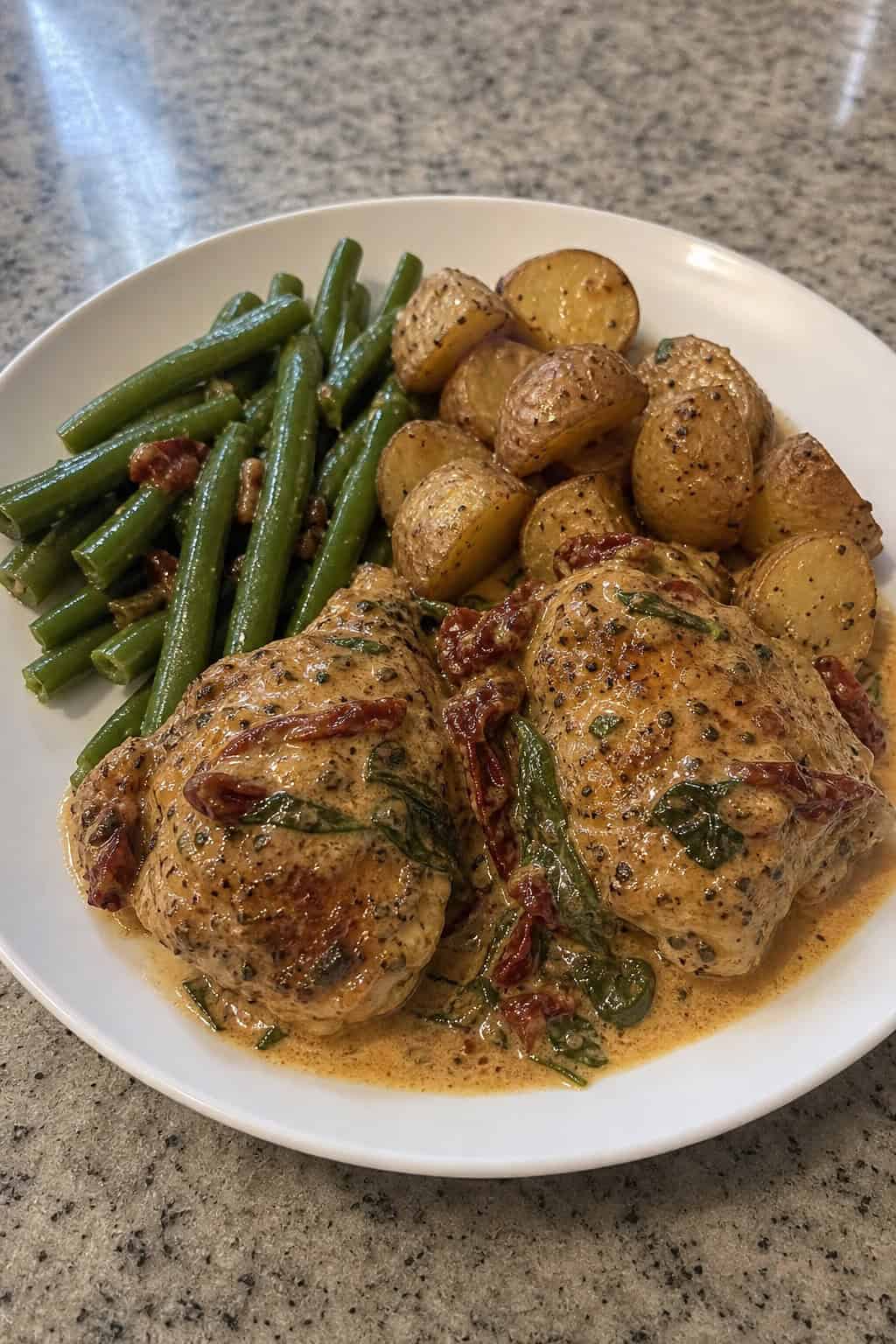 25 Chicken Thigh Recipes for Easy Weeknight Dinners 6 A plate of creamy Tuscan sun-dried tomato chicken thighs with green beans and roasted potatoes on a wooden table.