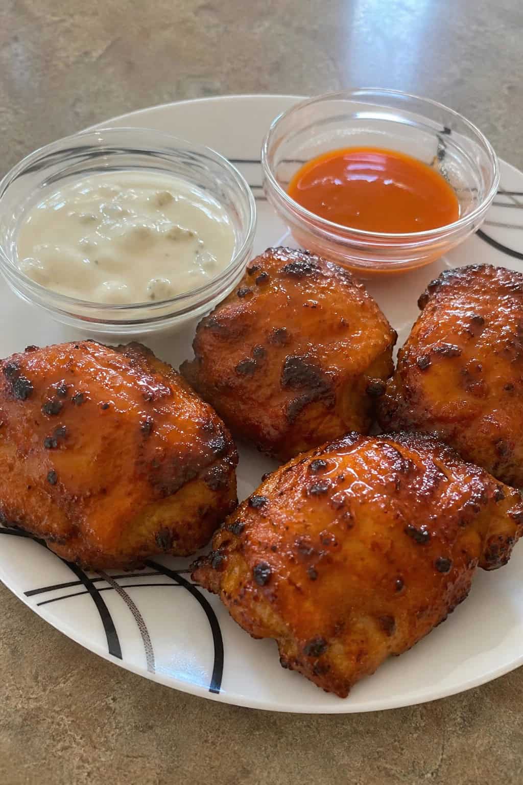 Close-up of crispy buffalo chicken thighs on a wooden board with celery sticks and dipping sauces.