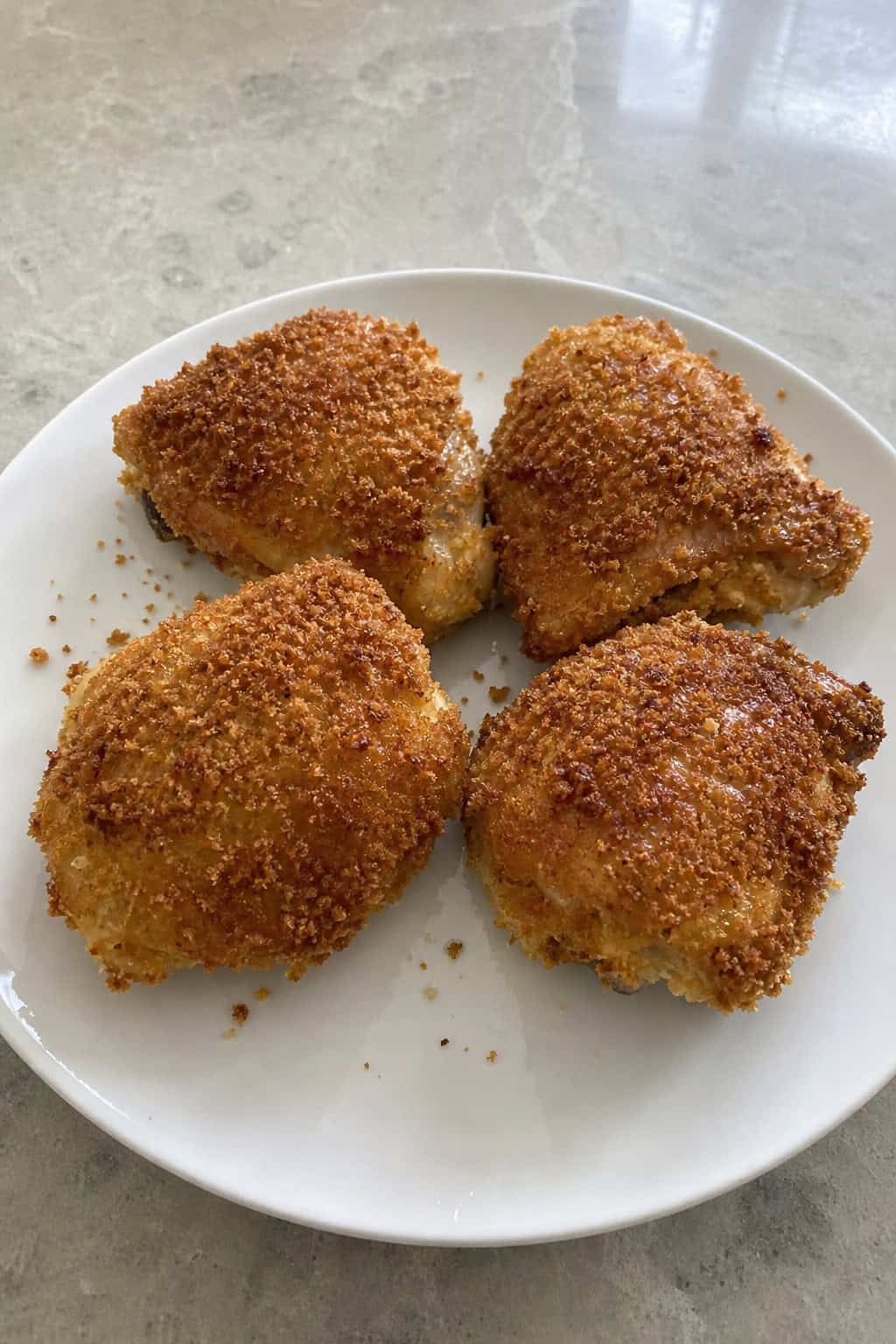 Golden-brown panko-crusted chicken thighs on a wooden board, garnished with a lemon wedge and sprigs of fresh herbs, showing a deeply crisped exterior.