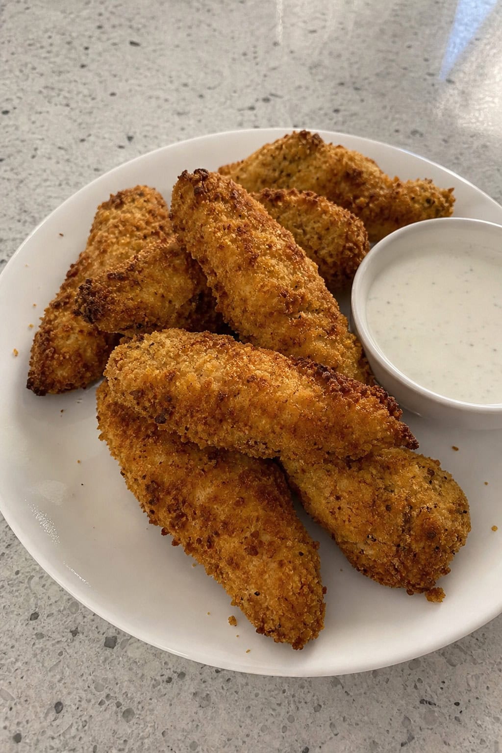 Plate of crispy air fryer chicken tenders with ranch dipping sauce and fresh parsley on a kitchen table.