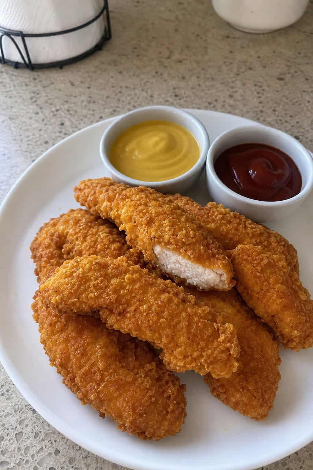 A plate of crispy cornflake chicken tenders with dipping sauces on a wooden table.
