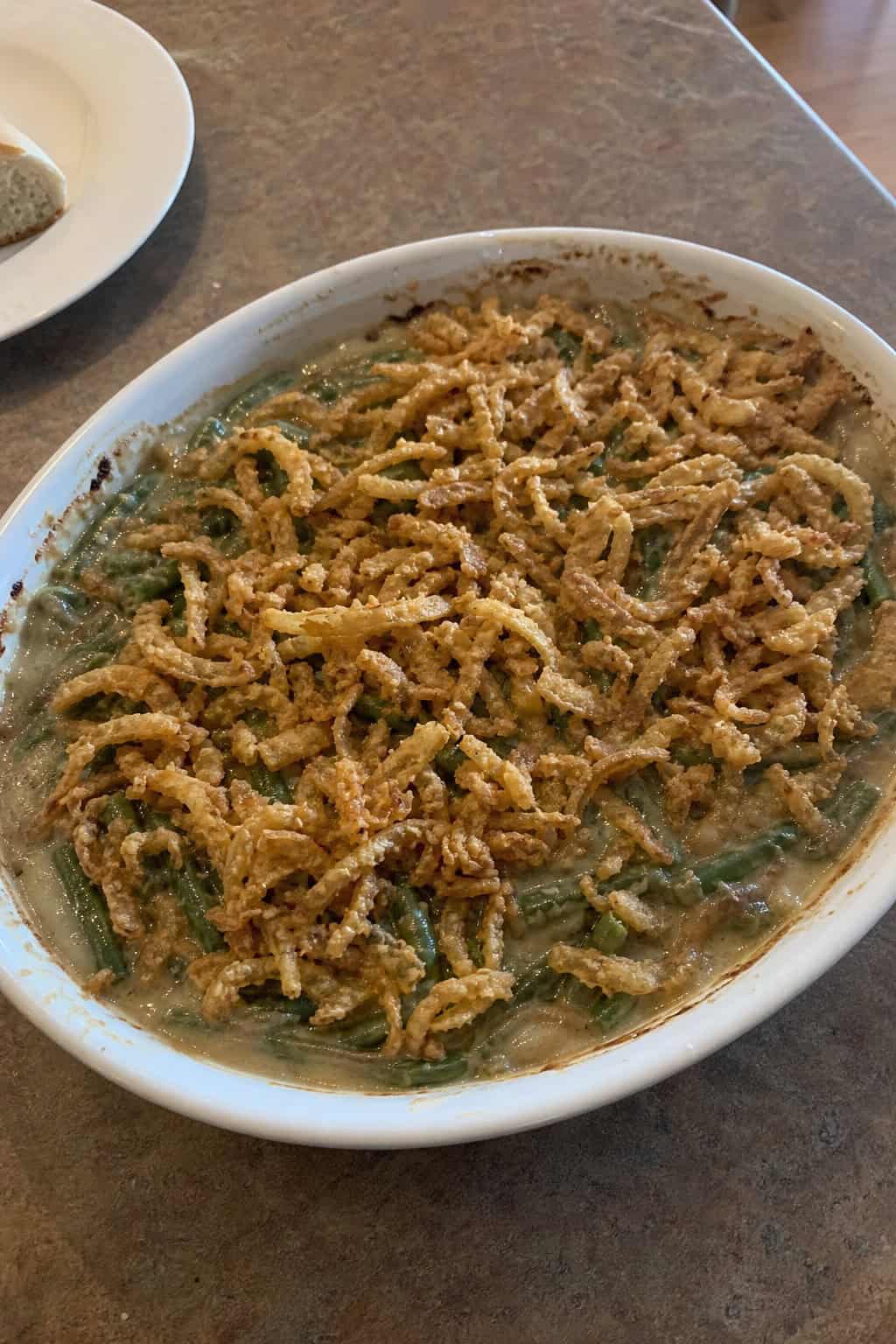 A baked green bean casserole with a thick layer of golden crispy fried onions piled high on top, served in a wide ceramic dish on a wooden table.