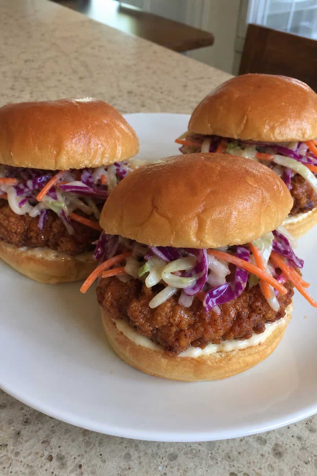 Three crispy minced chicken sliders with colorful quick slaw on a wooden board in a casual dining setting.