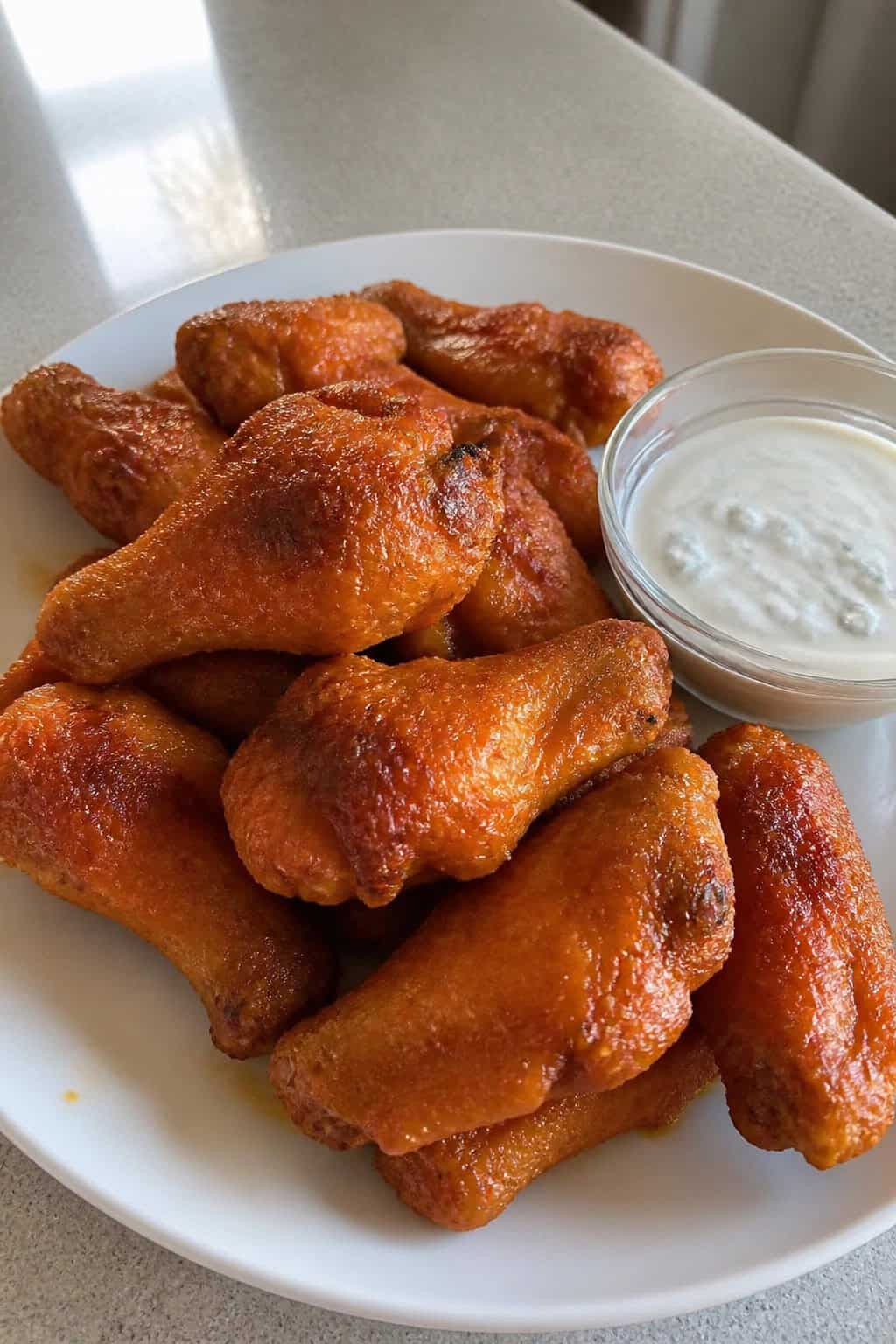 A plate of crispy buffalo chicken wings with a bowl of blue cheese dip, celery sticks, and carrot sticks on a wooden table.