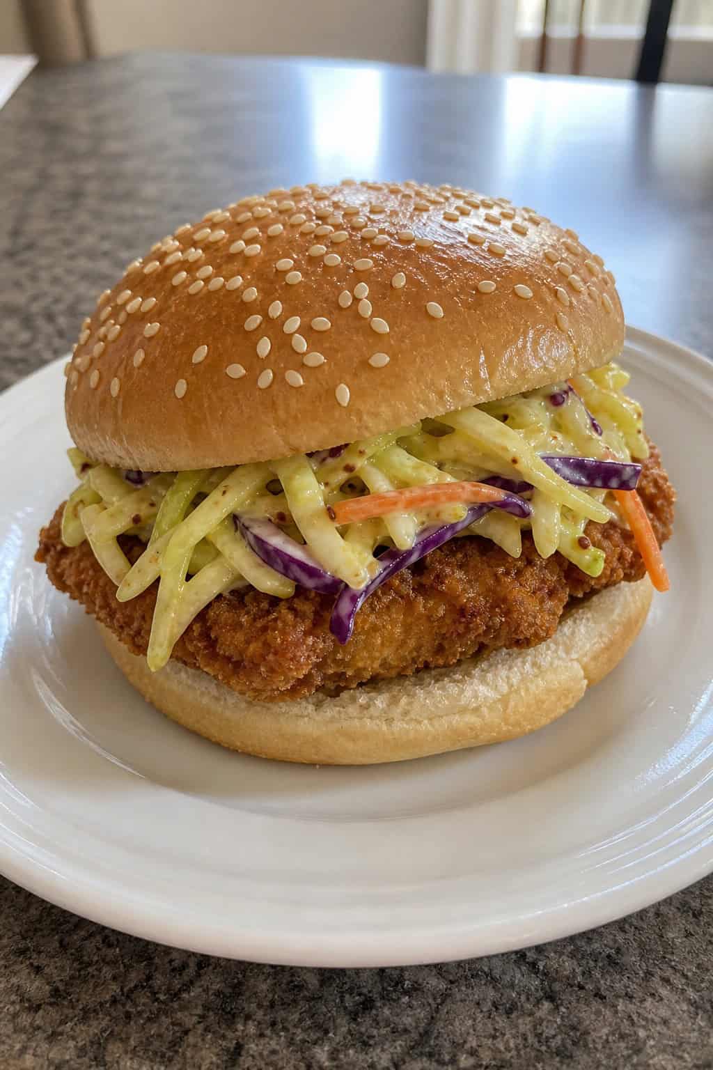 A panko-crusted oven-fried chicken sandwich on a wooden board with a ramekin of honey mustard sauce and shredded slaw visible on the side
