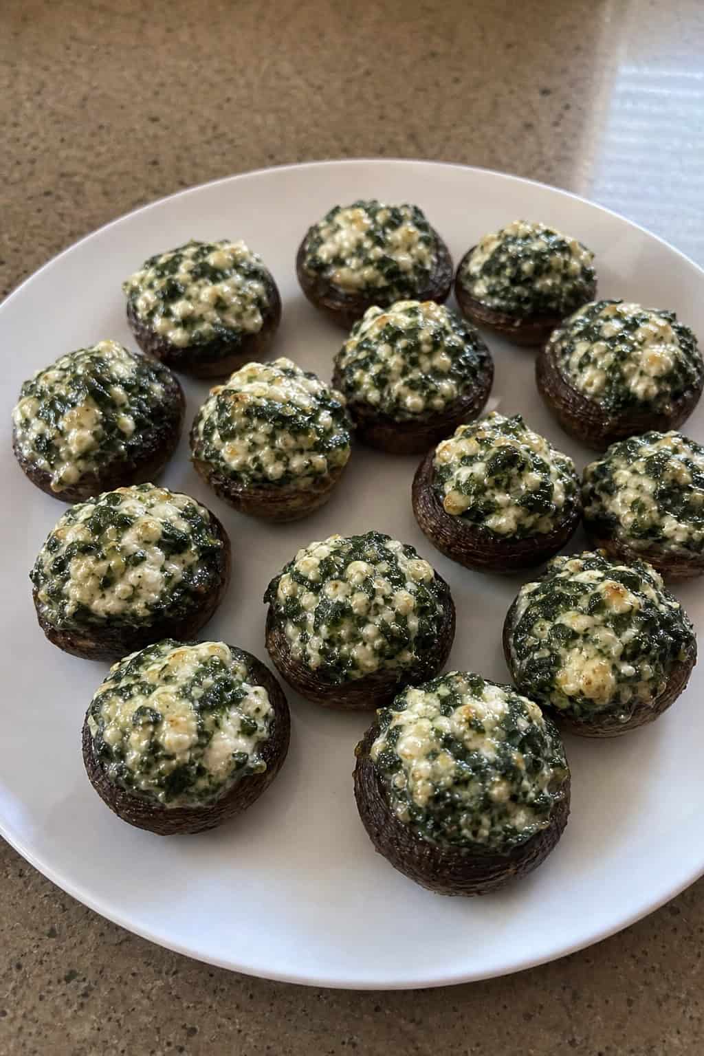A plate of spinach and feta stuffed mushrooms on a wooden table with garnish and a serving spoon nearby.