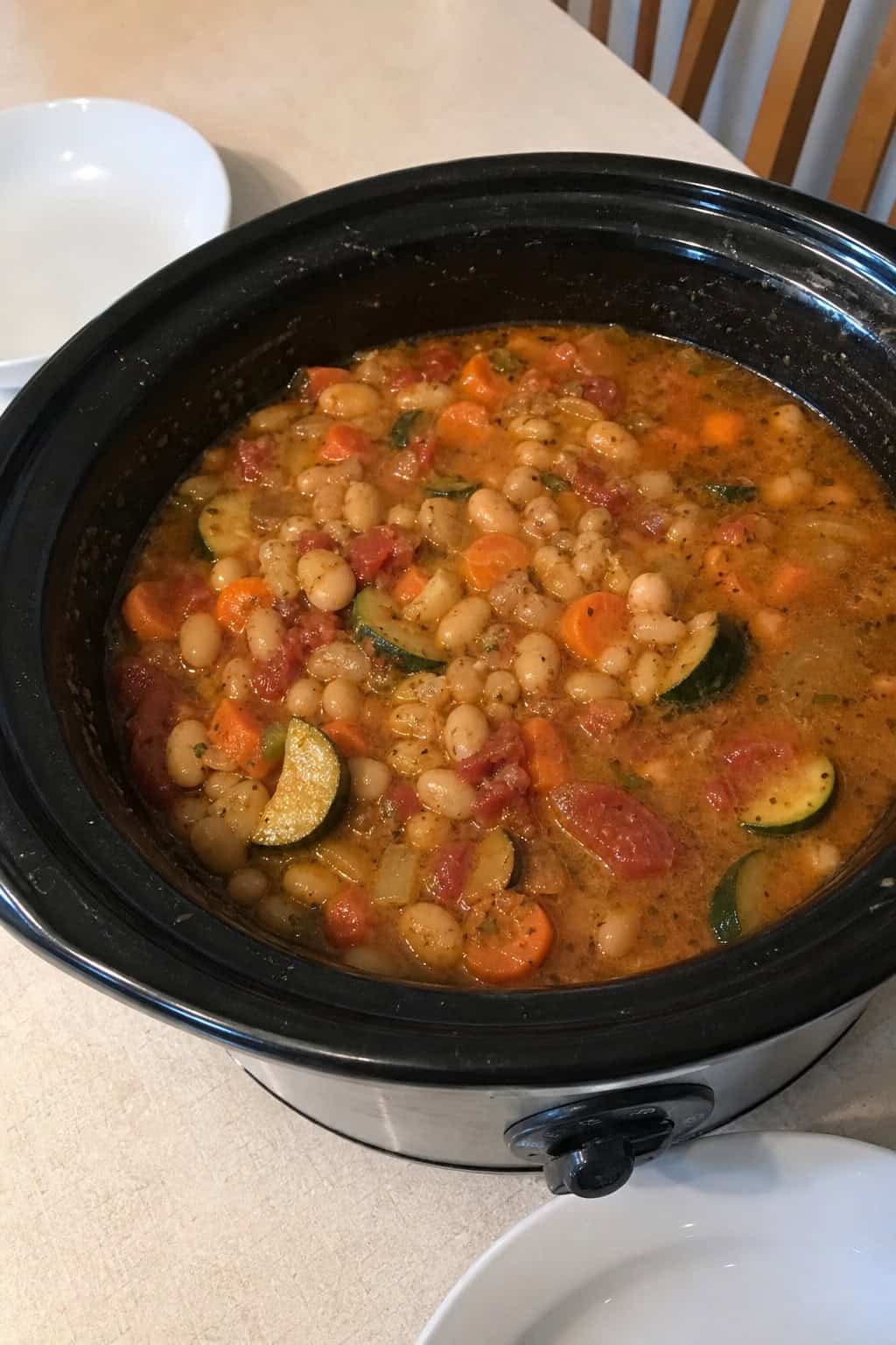 A crockpot filled with Mediterranean white bean stew on a kitchen table surrounded by fresh ingredients.