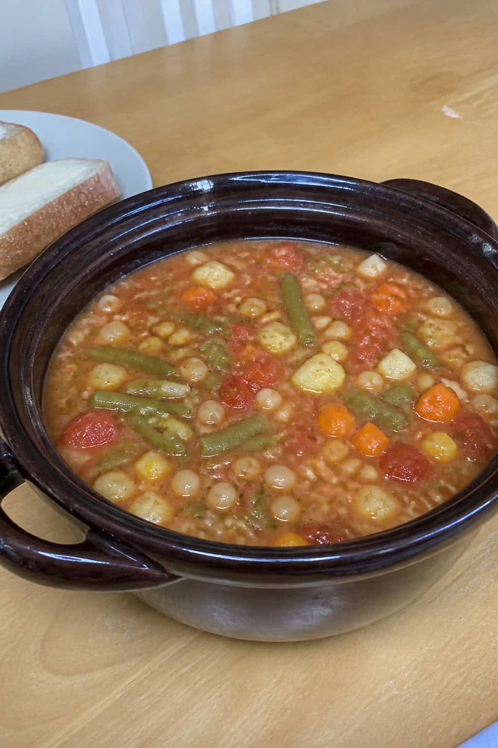 A crockpot filled with summer vegetable minestrone soup surrounded by fresh vegetables on a wooden table.